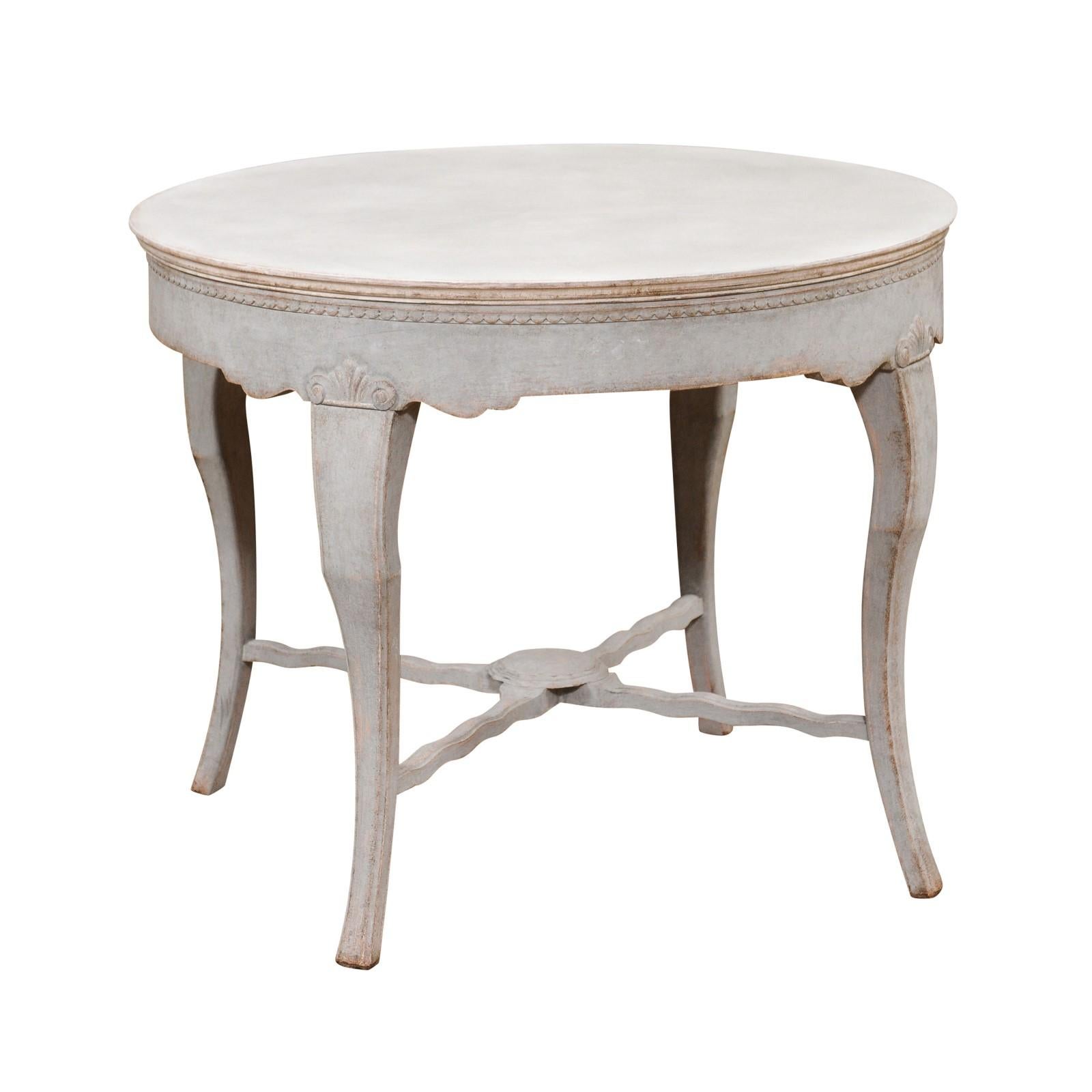 A Swedish gray painted table from the 19th century with circular top, carved beads, cabriole legs and X-Form stretcher. This 19th-century Swedish gray painted table exudes timeless charm and craftsmanship. Its circular top, adorned with delicately