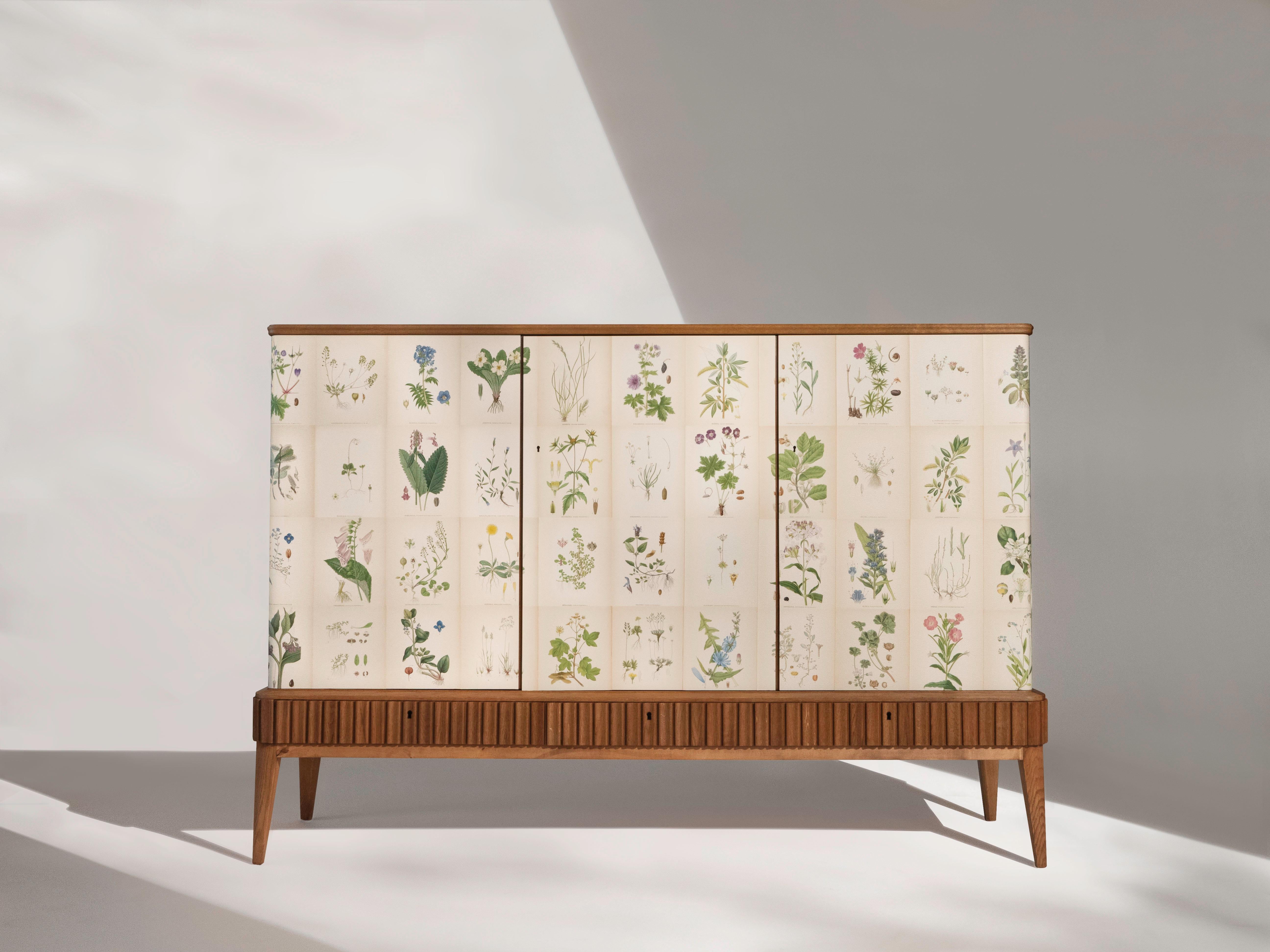 A Swedish 3-door sideboard or cabinet in oak with a mahogany top, circa 1950's. The rectangular cabinet is covered with the 1920's Norden's Flora Illustrations by C.A. Lindman.

The cabinet has three doors that conceal 2 compartments. The smaller