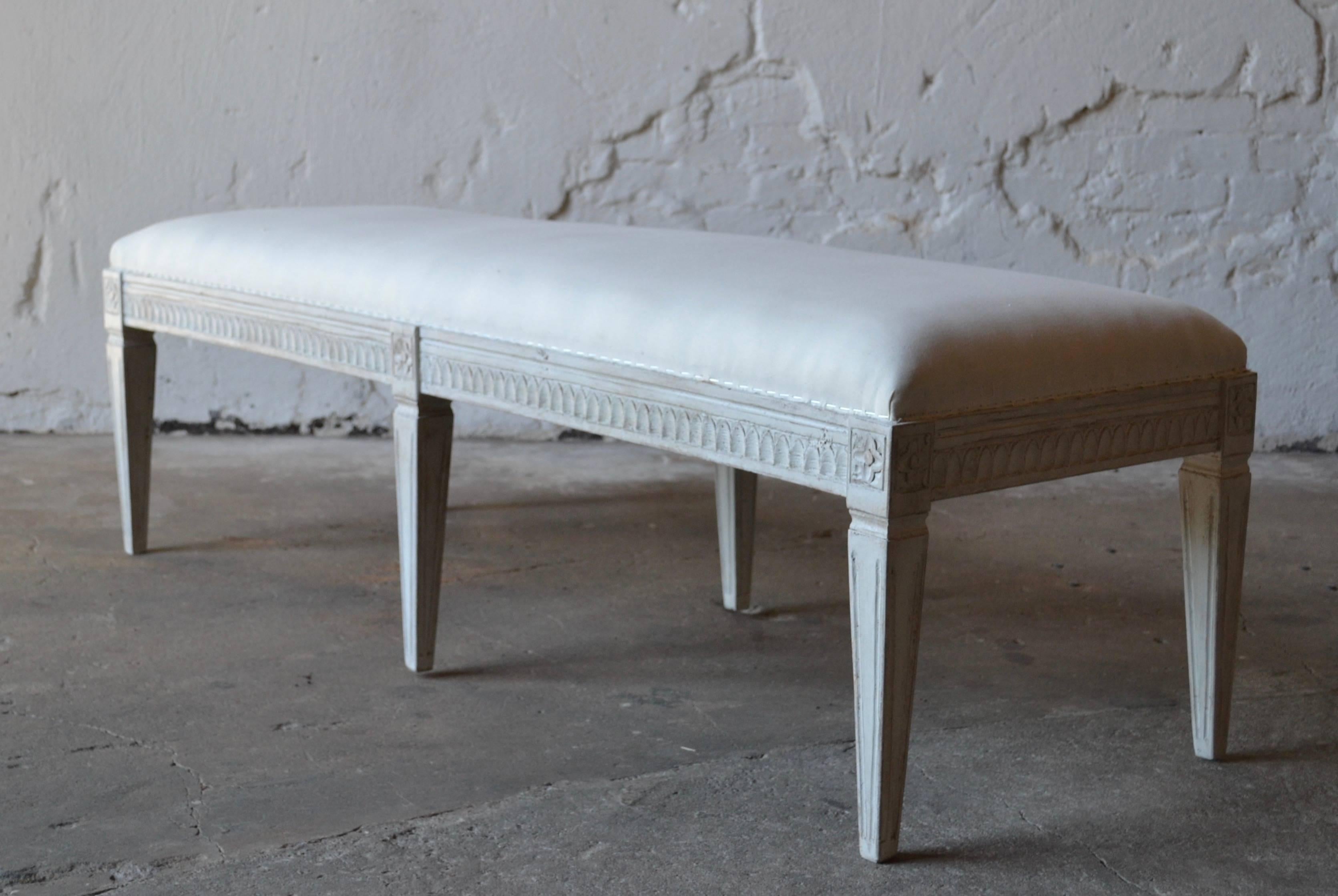 Antique Swedish Gustavian painted bench, with carved lamb's tongue apron, square tapered legs with carved flower rosettes at top of each leg. The bench is painted in a white-greyish color and distressed finish.
Renewed upholstery and textile.

 