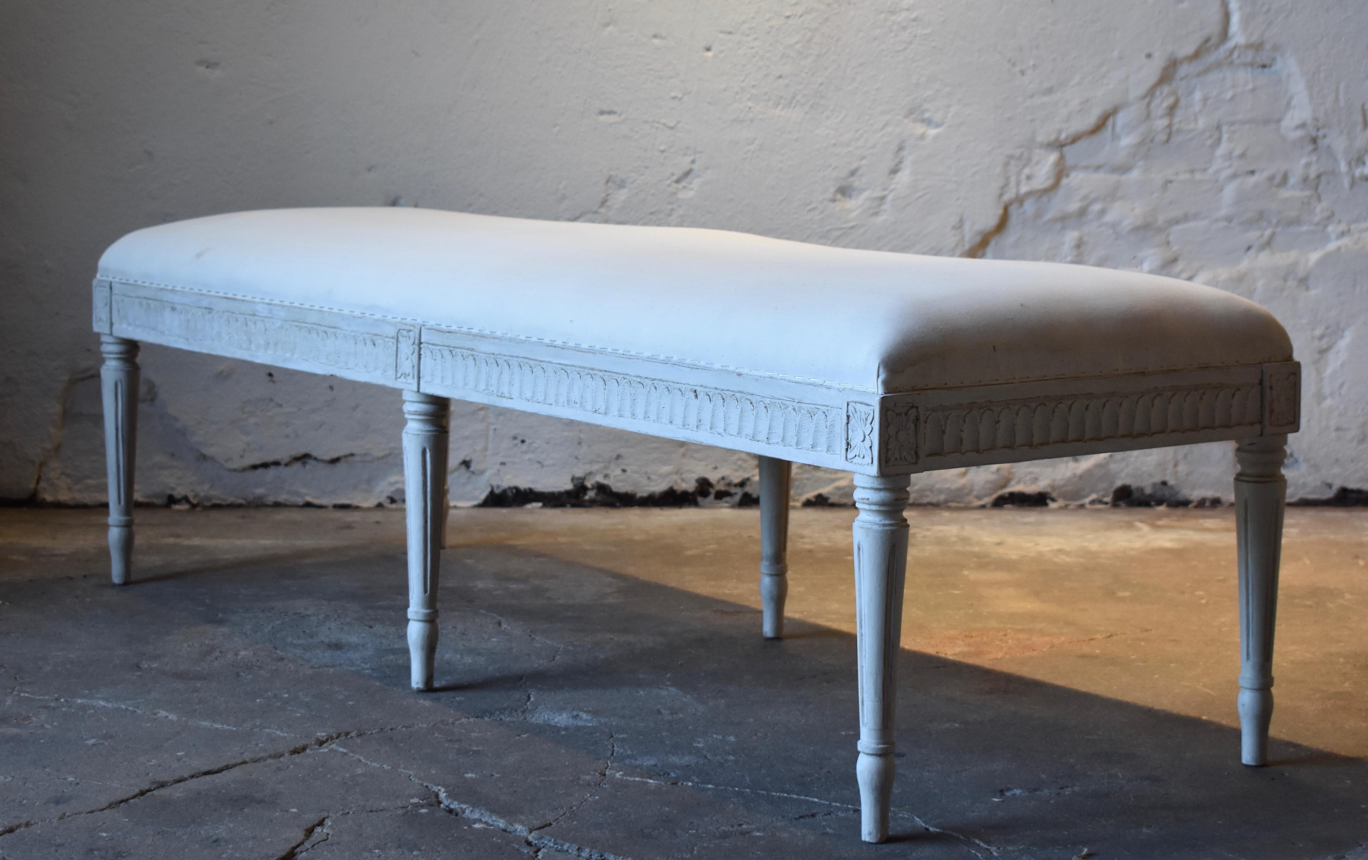 Antique Swedish Gustavian painted bench, with carved lamb's tongue apron, square tapered legs with carved flower rosettes at top of each leg. The bench is painted in a white-greyish color and distressed finish.
Renewed upholstery and textile.

  