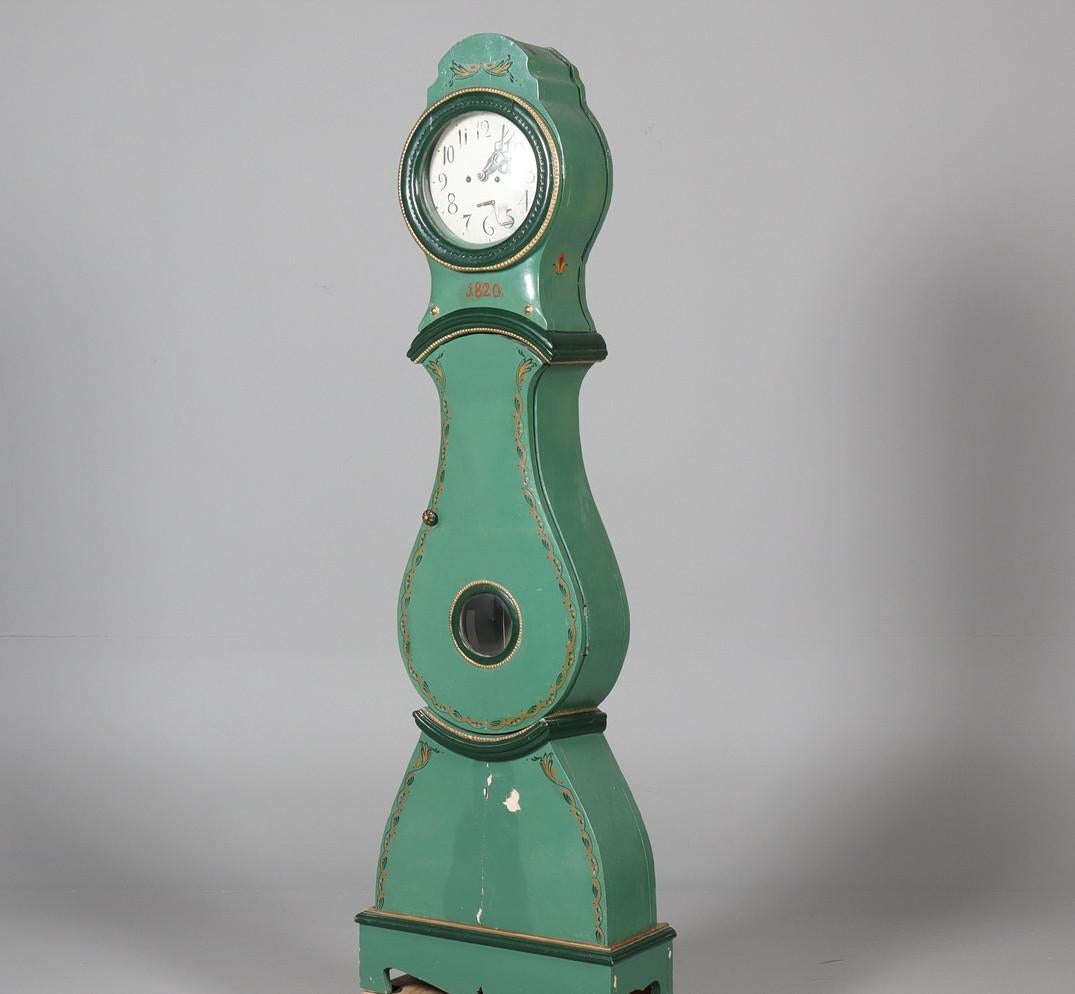 192cm  early 1800s antique Swedish mora clock with carved detail on the hood  in a green paint finish and detailed face and hand painted detailing.

Measures: 192cm.

The clock body is distressed as befits its age and has the usual wood movement