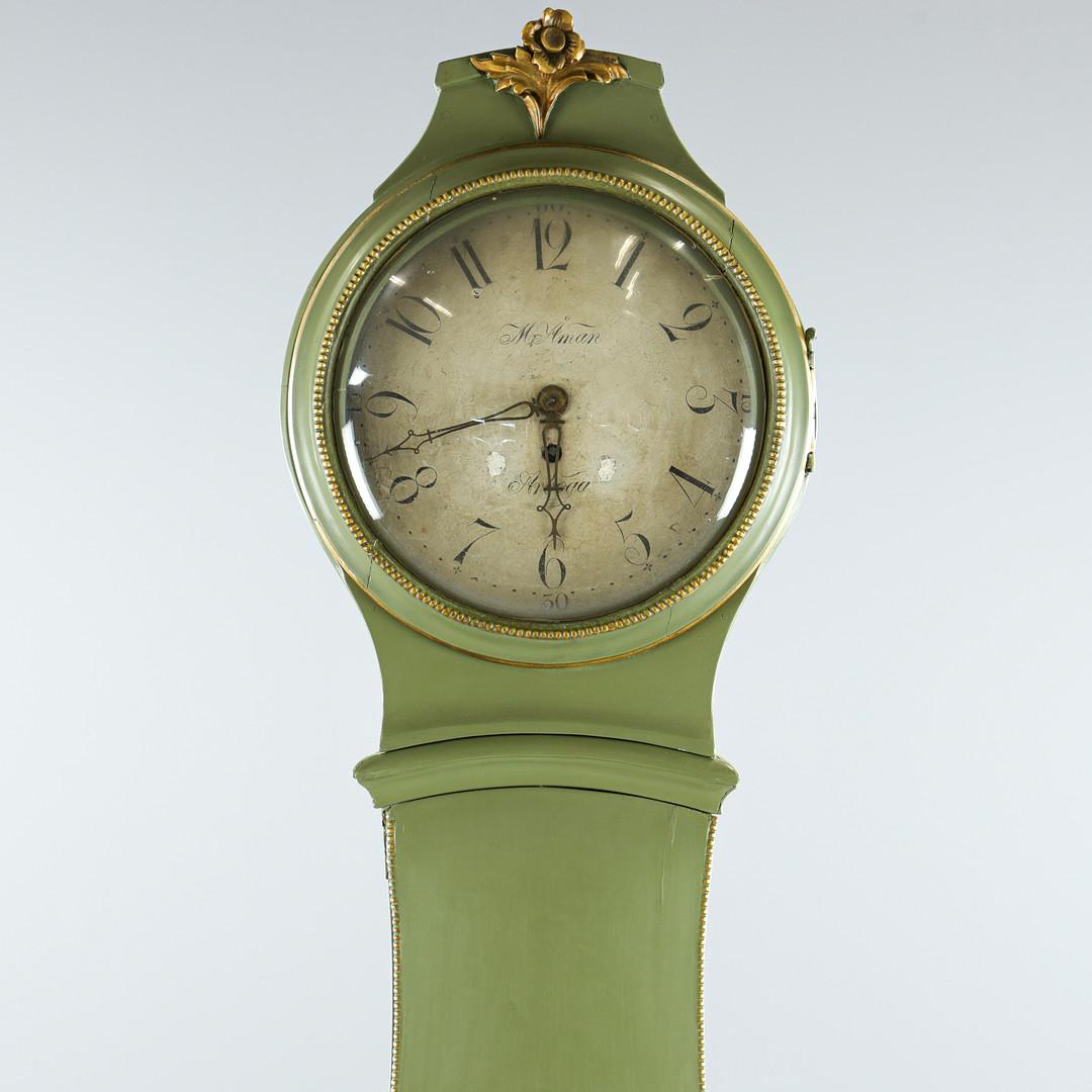 210cm  early 1800s antique Swedish mora clock with carved detail on the hood  in a green paint finish and detailed face and hand painted detailing. Maker Named Åman, Arboga on face

Measures: 210cm.

The clock body is distressed as befits its age