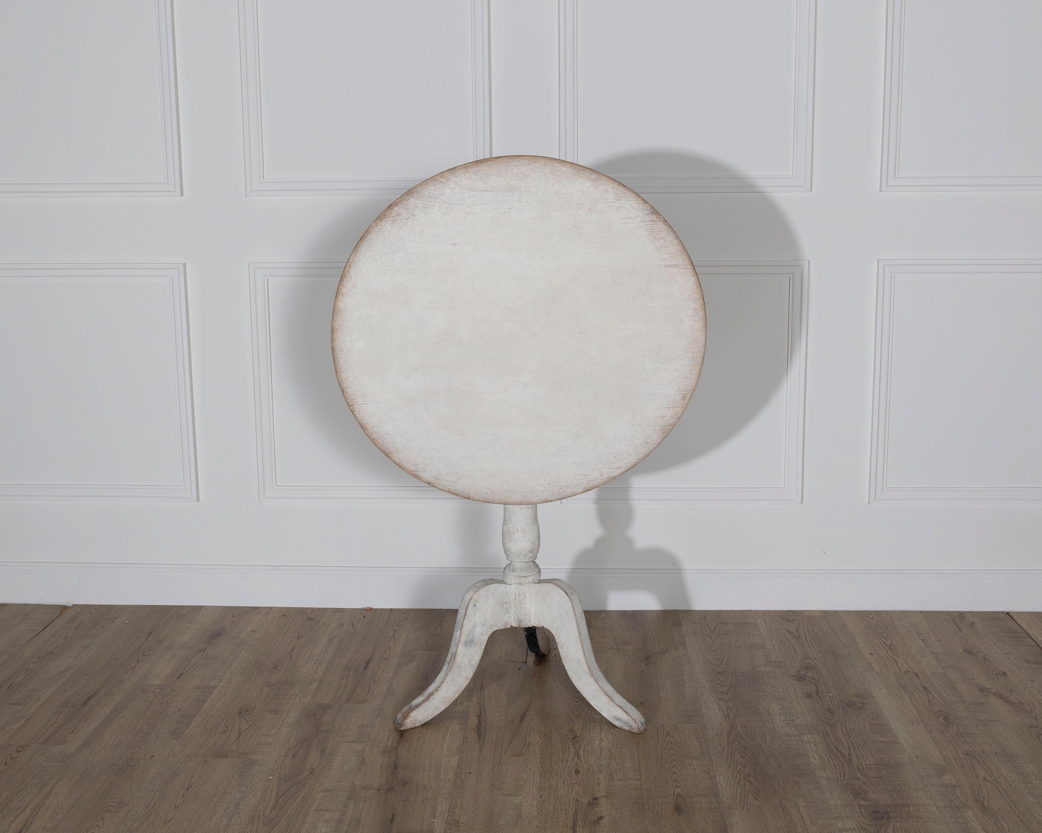 A graceful Swedish antique tilt-top table dating to the late 19th century, showcasing the quiet charm and simplicity of rural Nordic design. Crafted from pine and painted in a soft, timeworn white, this round table features a classic tilt-top