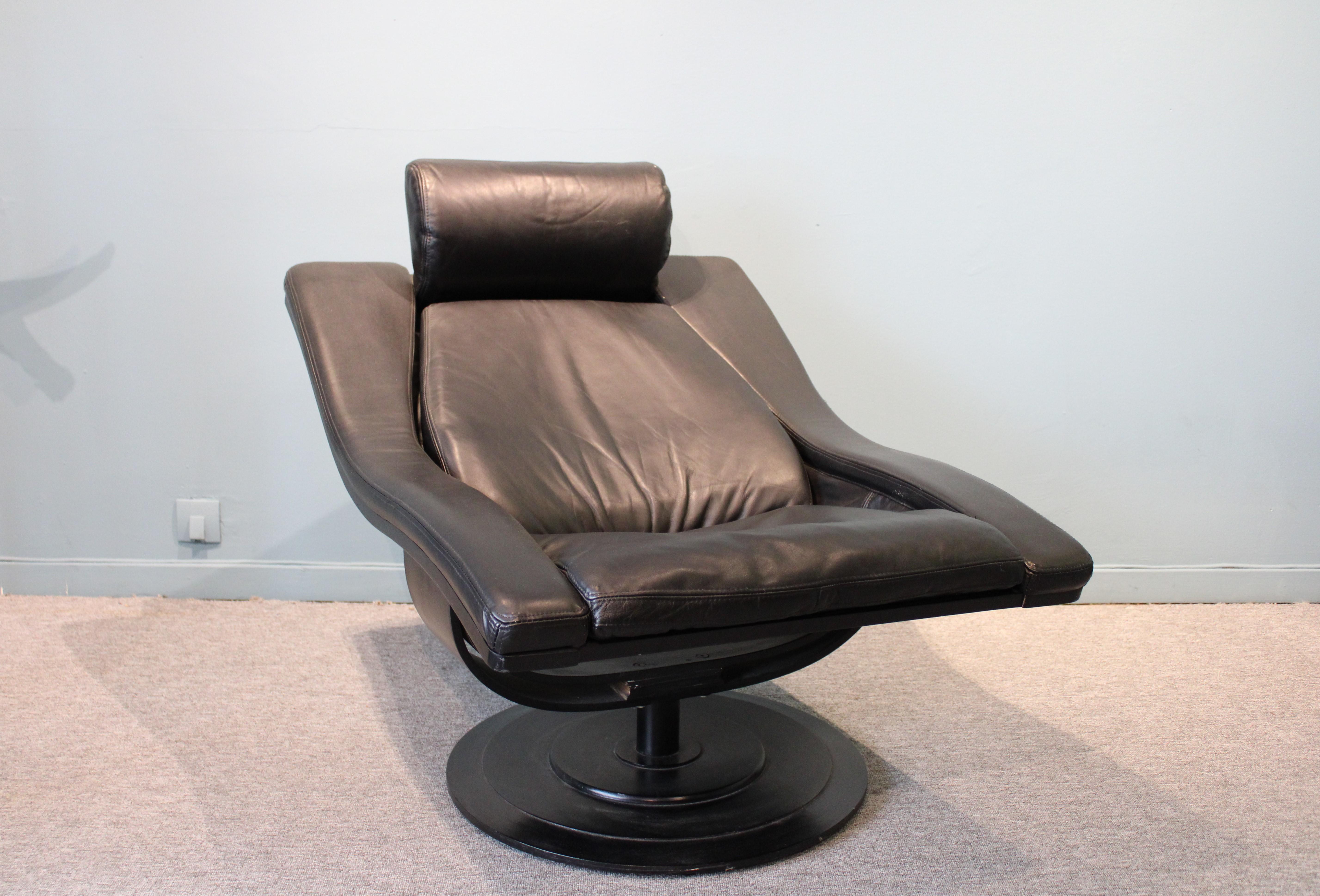 Swivel armchair and ottoman in black leather, structure in black painted wood.
By Akamura and Marquadsen for Nelo. Swedish, 1970s.
Measures: Armchair 100 x 75 x H 80 cm. 
Ottoman 45 x 50 x H 38cm.