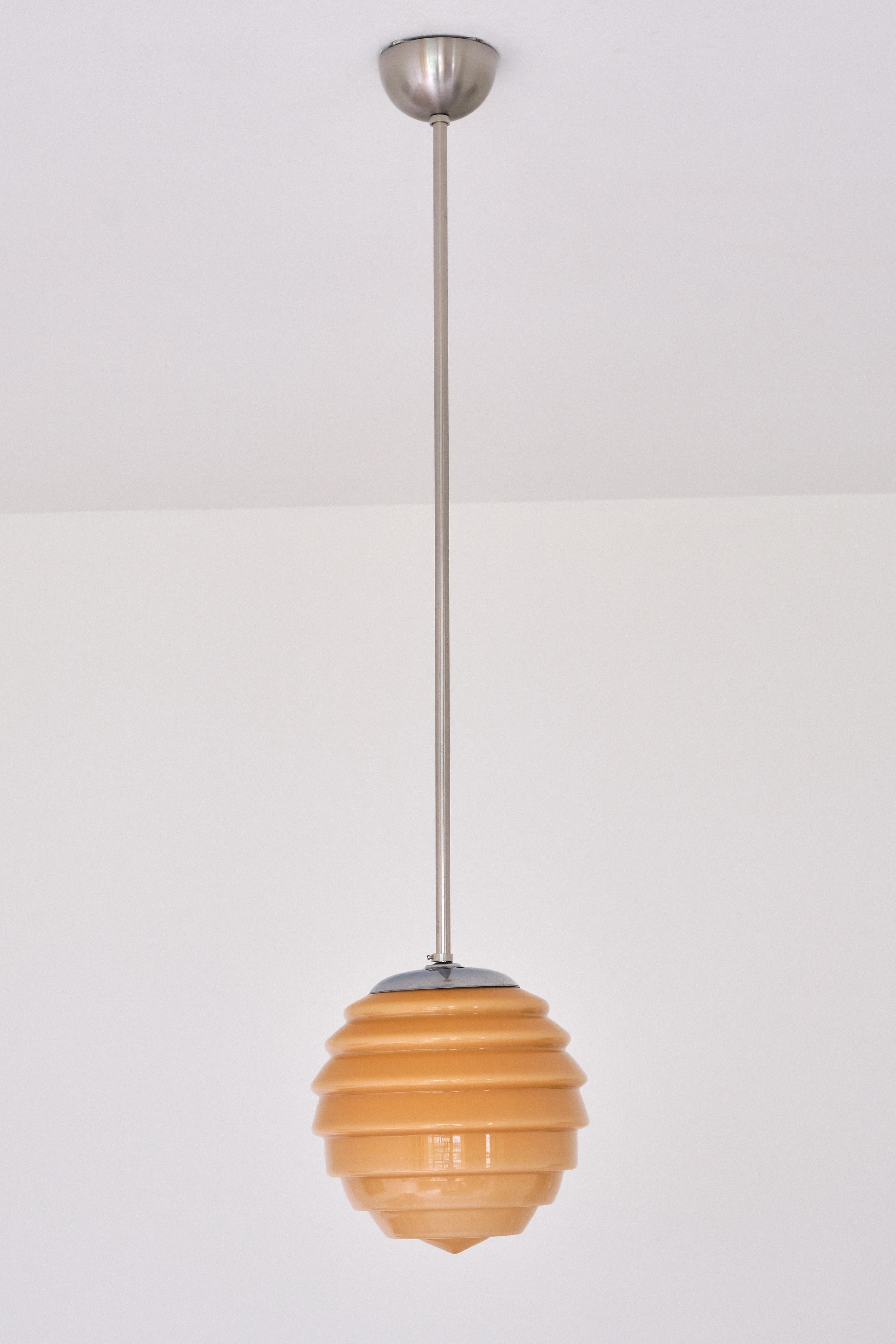 This elegant pendant light was produced in Sweden in the 1930s. The design is marked by the striking beehive shape of the glass shade. The tiered shade is made of a light peach orange glass in a very subtle gradient. When illuminated, the lamp