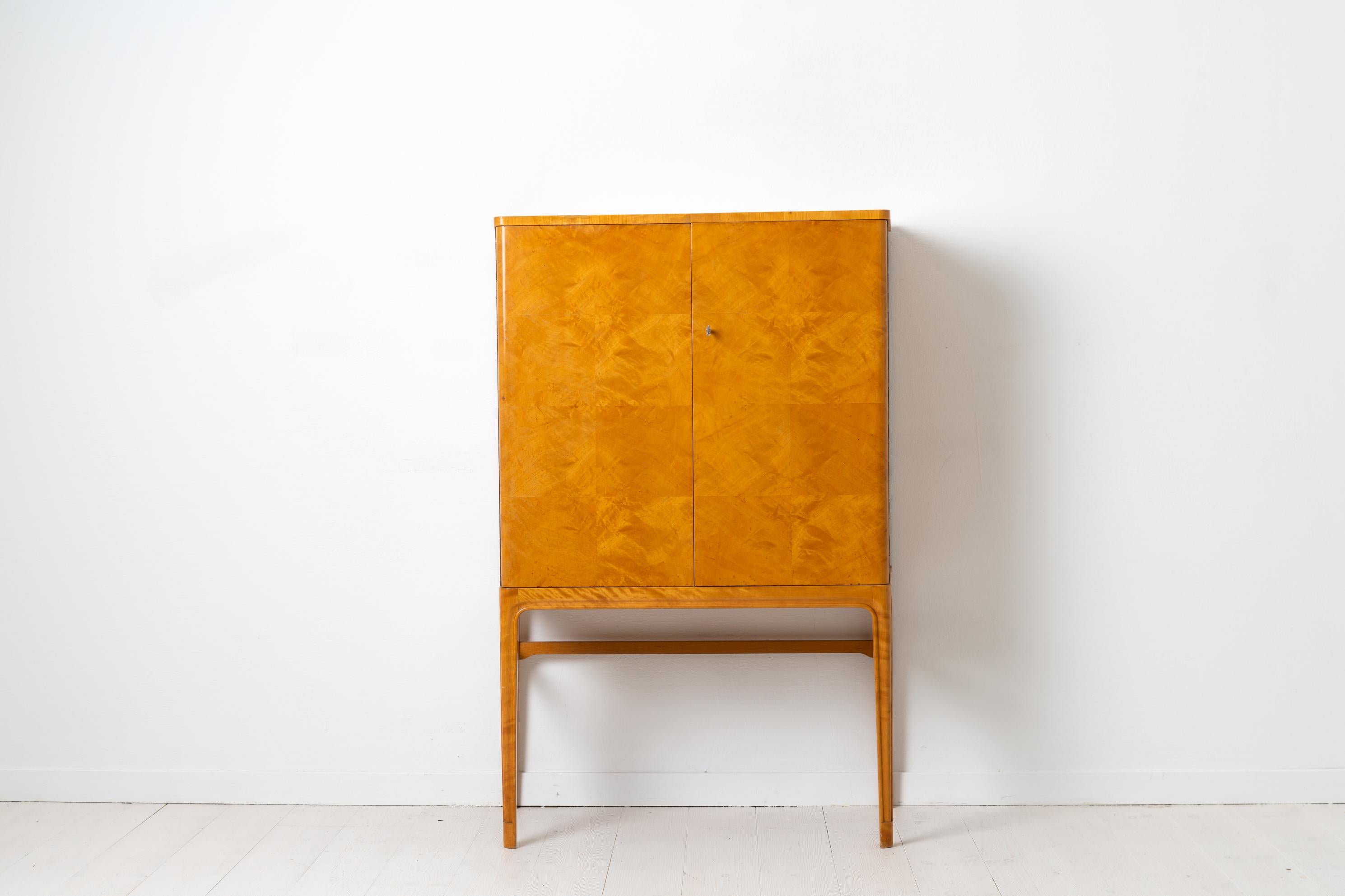 Swedish Art Deco cabinet with an exterior in veneered light birch and with an interior of mahogany. The interior has one shelf and 2 thin drawers with the rich mahogany color contrasting with the lighter exterior birch. The cabinet is vaguely