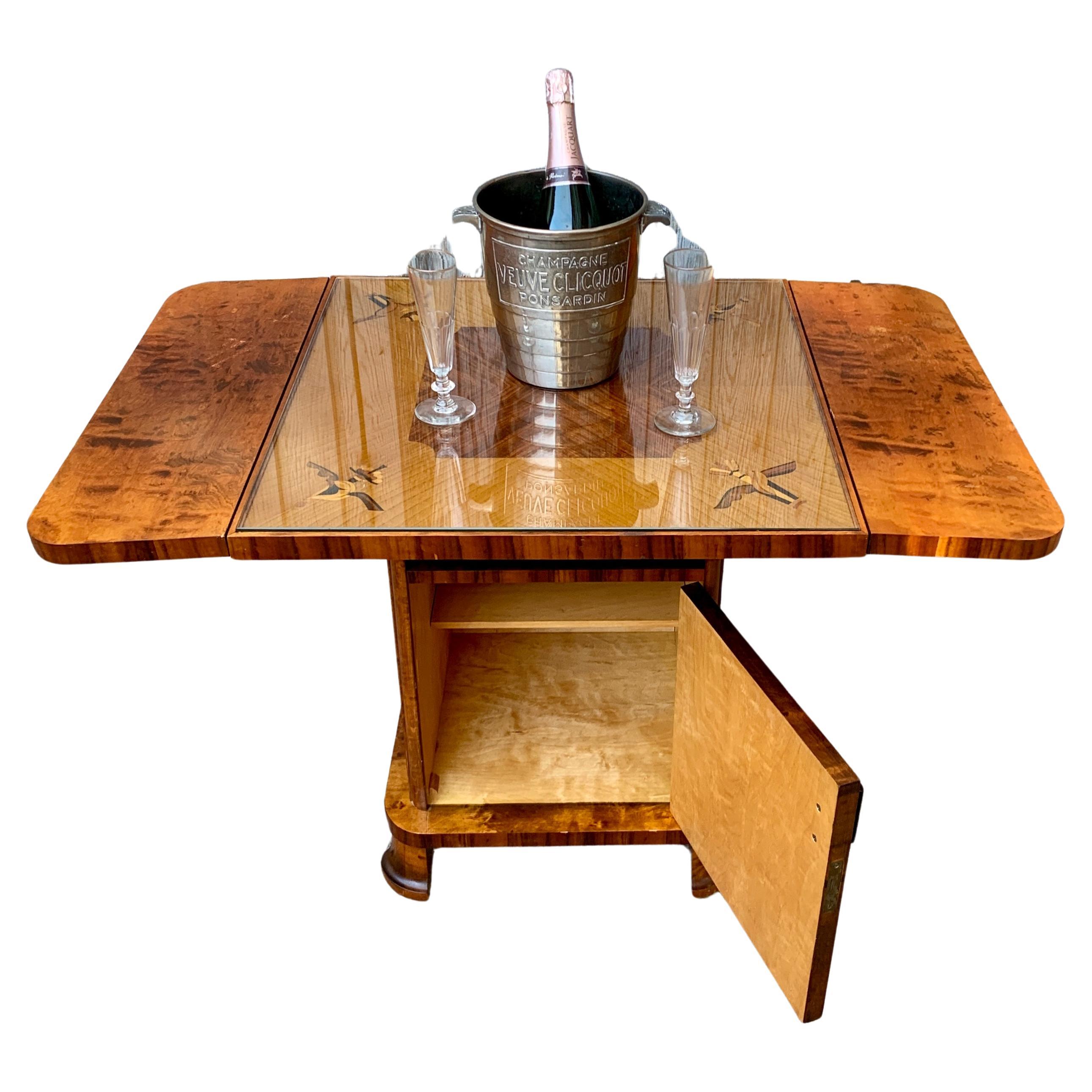 A Swedish free-standing cocktail table with two drop leaves. One side can  lift up or both at the same time. With one front door, bottles can be stored. A thick glass top that goes in without sliding away, has kept the top of this drop leaf table