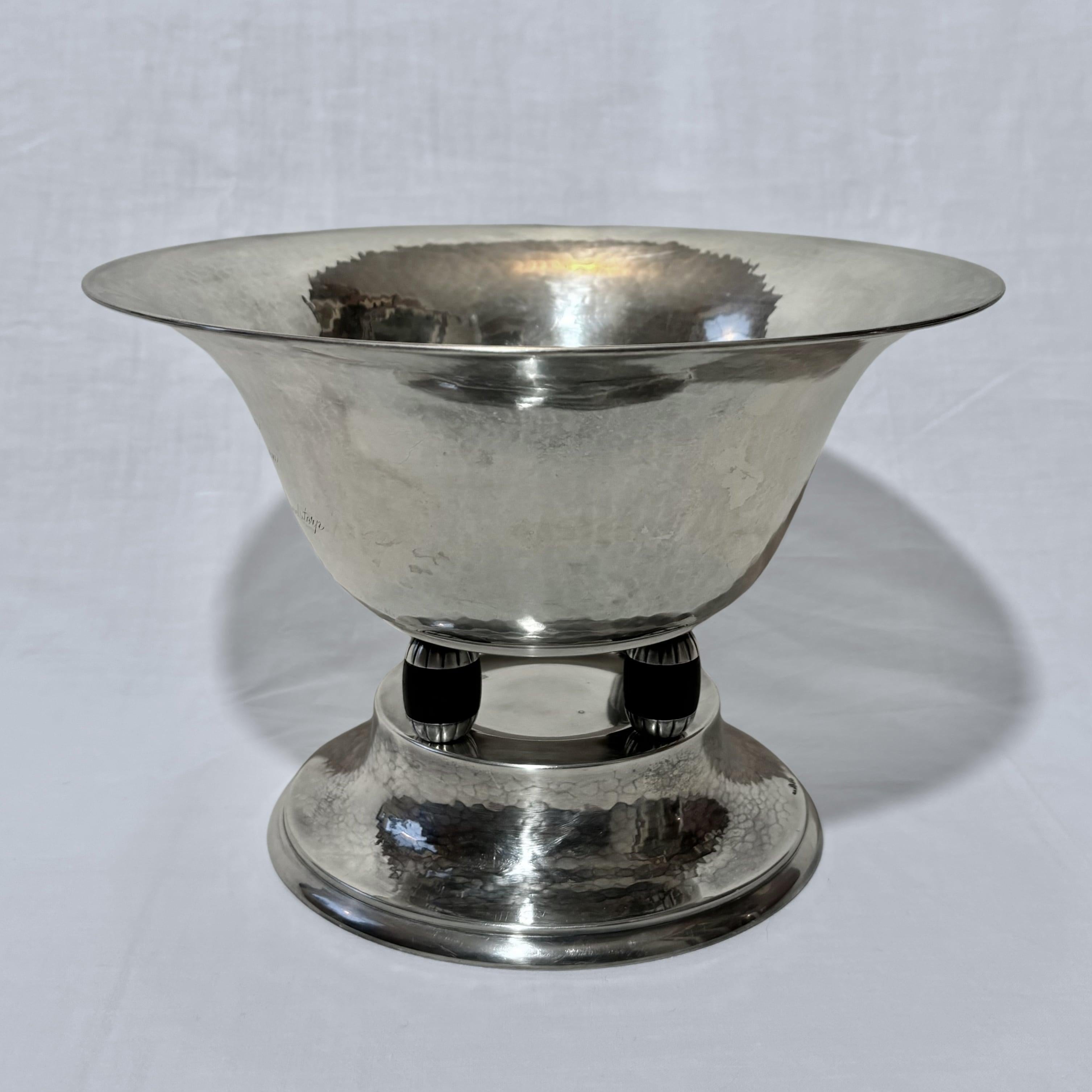 A graceful Art Deco bowl produced in the 1930s by Swedish maker Guldsmedsaktiebolaget (GAB) located in the town of Eskilstuna. This elegant piece is elevated by four black wooden pillars, creating a distinctive and striking silhouette. The bowl is