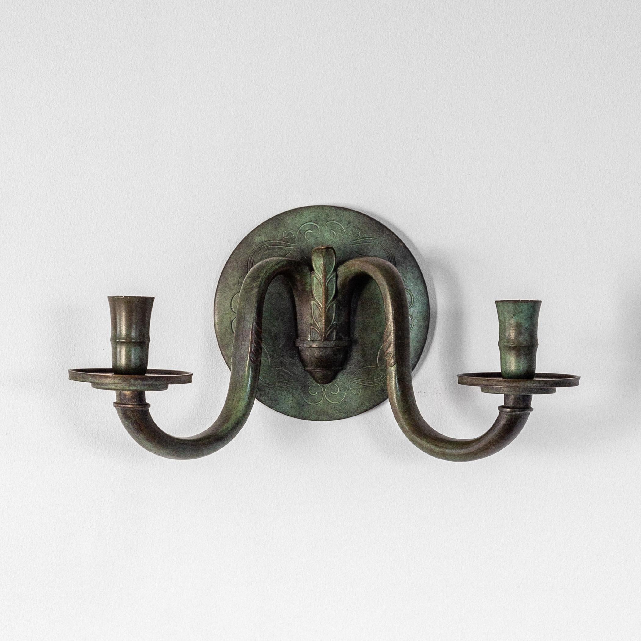 Applique svedese Art Deco a doppio braccio in bronzo, anni '20-'30 circa. Questo elegante candelabro da parete presenta una patinatura con ricchi toni verdi, caratteristica dei bronzi svedesi d'epoca. 
Il piatto posteriore circolare è splendidamente