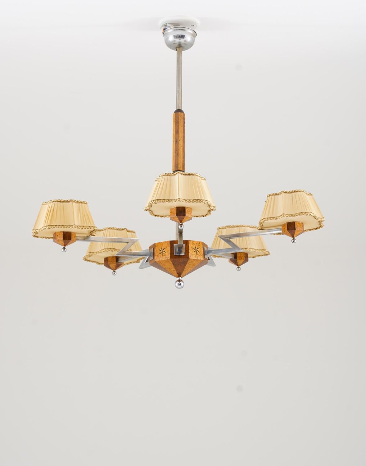 Questo lampadario svedese degli anni '30 è un ottimo esempio di design Art Deco con un'atmosfera calda e naturale. Realizzato con intarsi di betulla masur e radice di olmo, il mozzo centrale in legno presenta una forma sfaccettata con sottili motivi