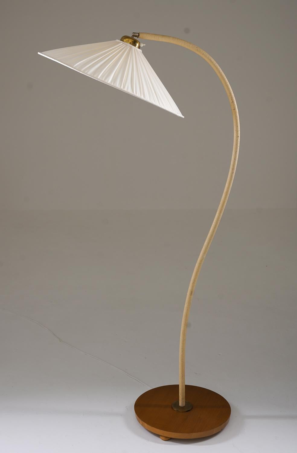 Swedish Art Deco floor lamp with a teak base and a gracefully curved gooseneck rod wrapped in hemp rope, creating a natural and tactile surface. The lamp features brass details, including a polished brass joint and lamp holder, which add a refined
