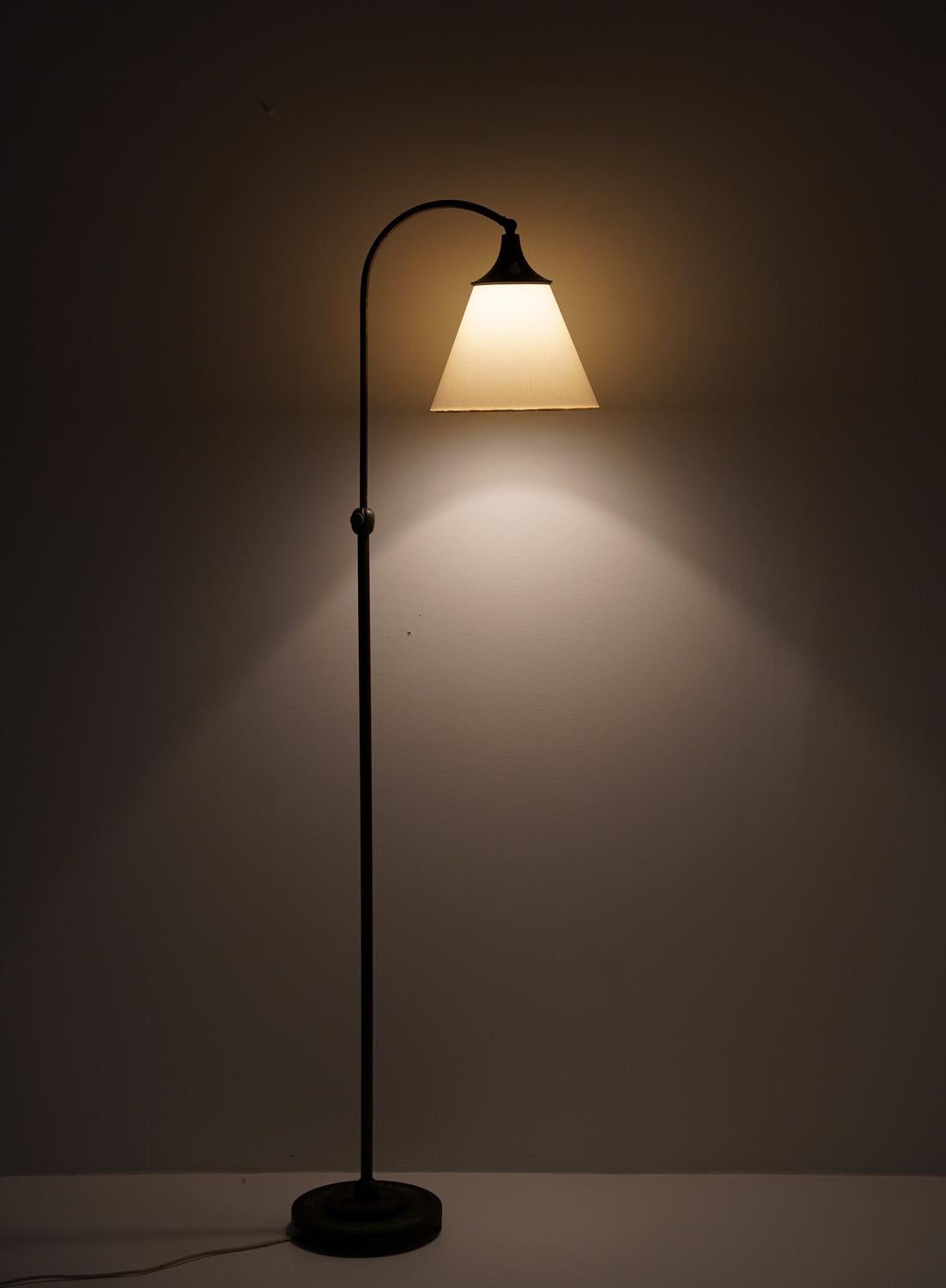 Hübsche Art-déco-Stehlampe, hergestellt in Schweden, 1920er Jahre. 
Die Leuchte besteht aus einem Sockel und einer Stange aus Bronze, die einen hakenförmigen Schwenkarm tragen, der den Schirm hält. Die Lampe hat ein halbminimalistisches Design mit