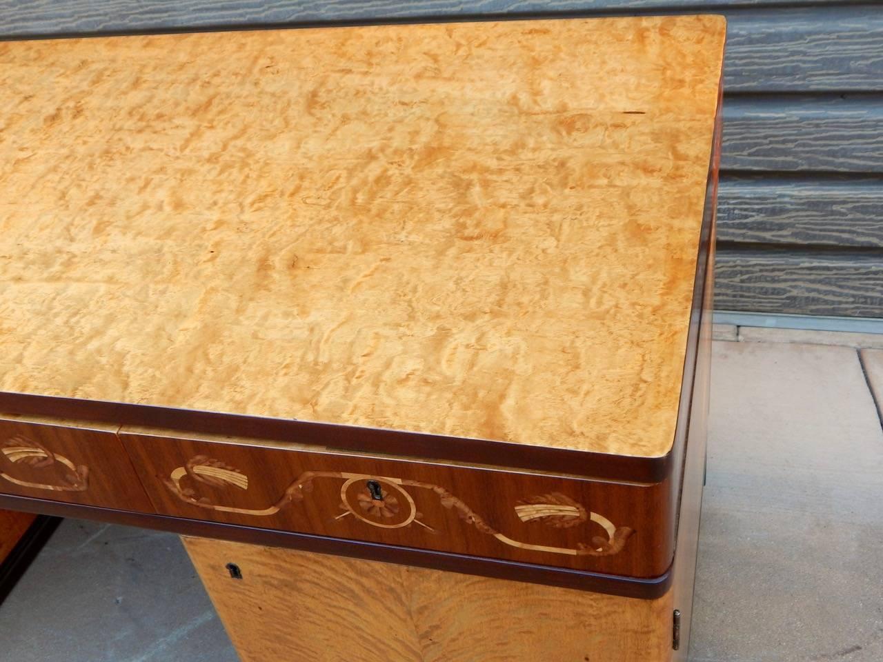 Swedish Art Deco inlaid desk made at Ferdinand Lundquist in Gothenburg, Sweden in the 1930s. Rendered in highly figured golden flame birchwood. Inlaid neoclassically inspired banding rendered in rosewood, Carpathian elm and birchwood. Ebonized birch