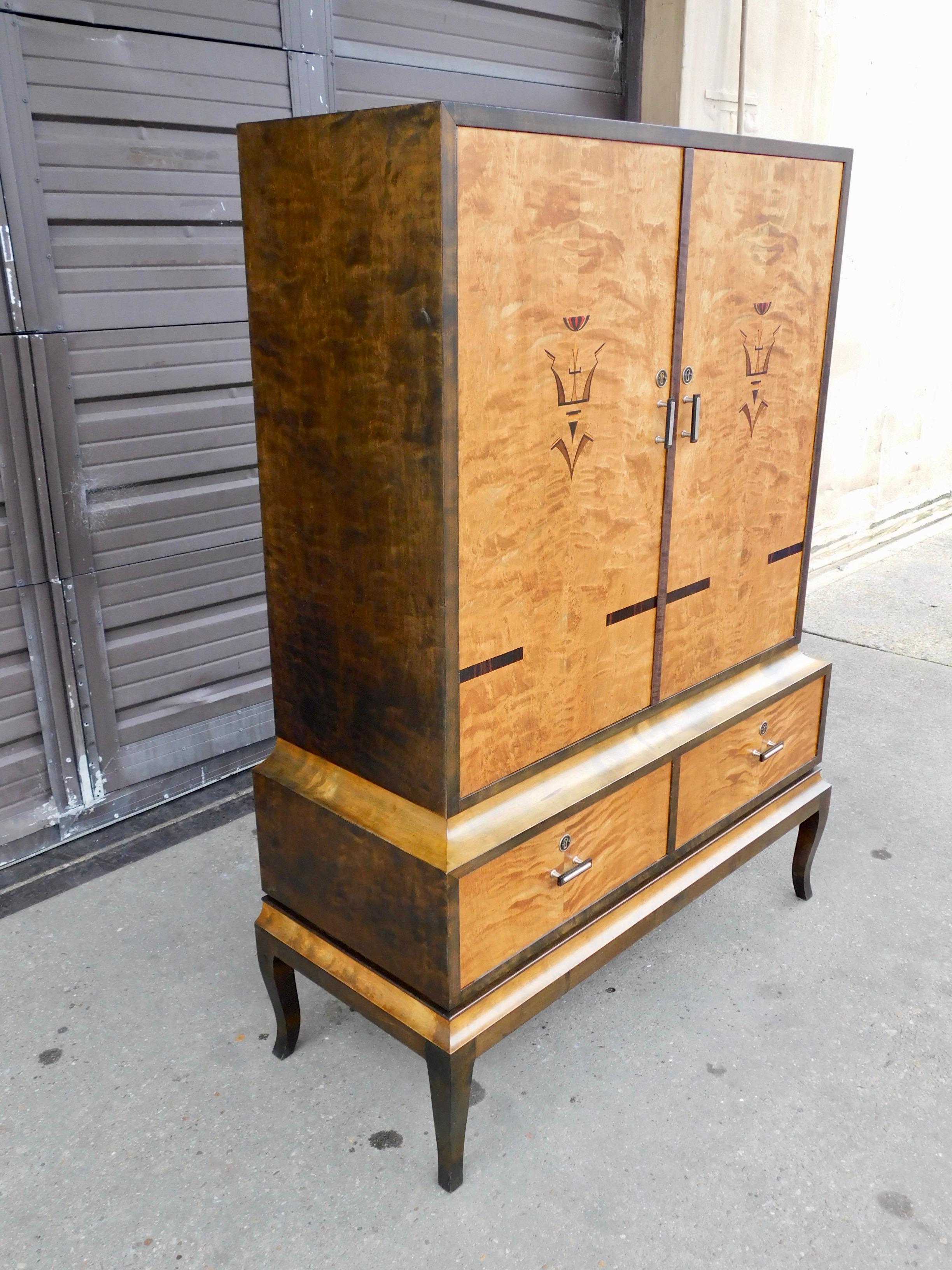 Swedish Art Deco inlaid storage cabinet rendered in birch wood. With doors in highly figured bookmatched birch wood. Inlaid on doors in rosewood and ebony. Case in dark stained birch wood. With two original shelves (solid birch wood) in the cabinet.