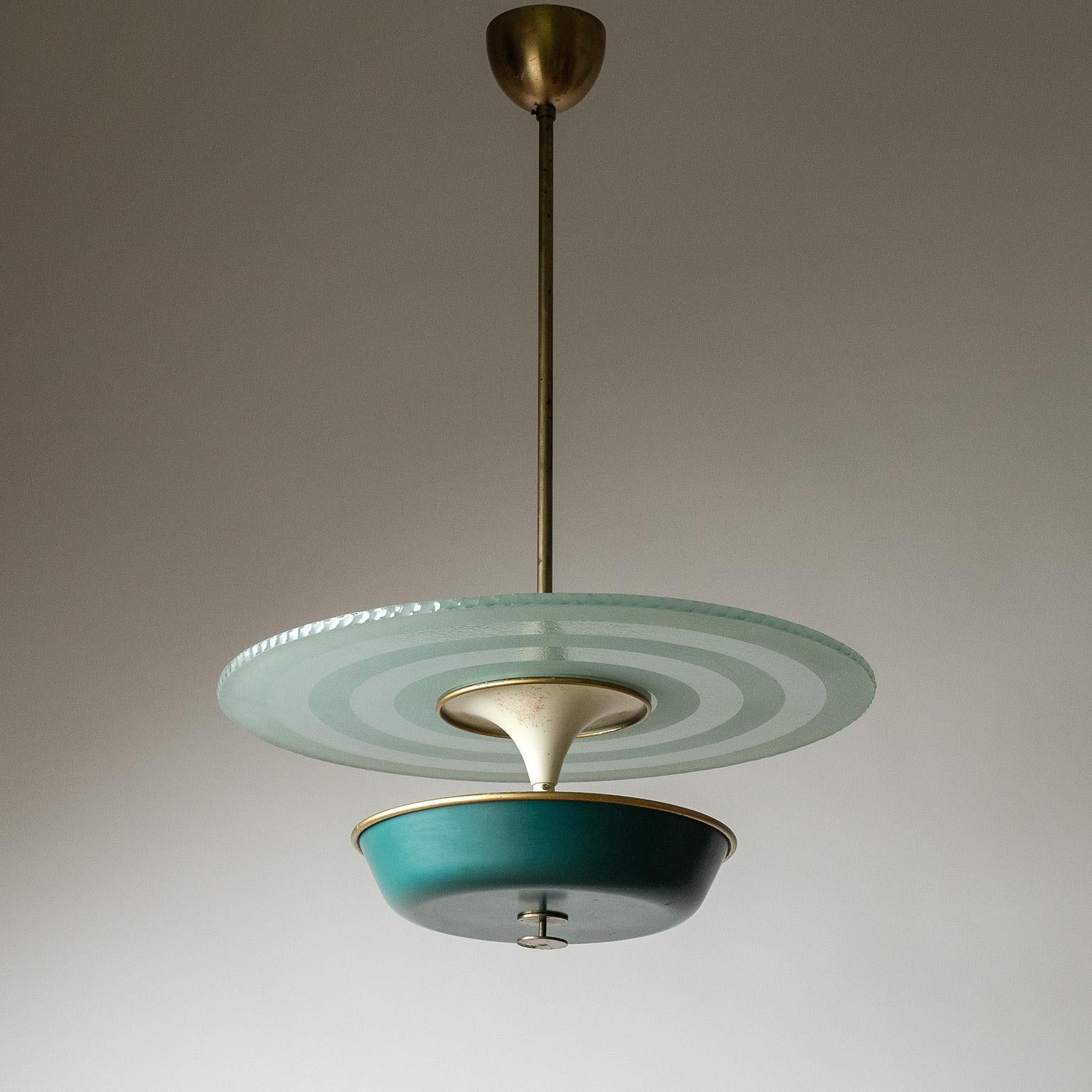 Graphical Swedish Art Deco pendant from the 1930s, possibly by Böhlmarks. A forrest-green lacquered shade and a large „raw glass“ disc-diffuser with a chipped edge and frosted concentric circles. The position of the glass can be altered along the