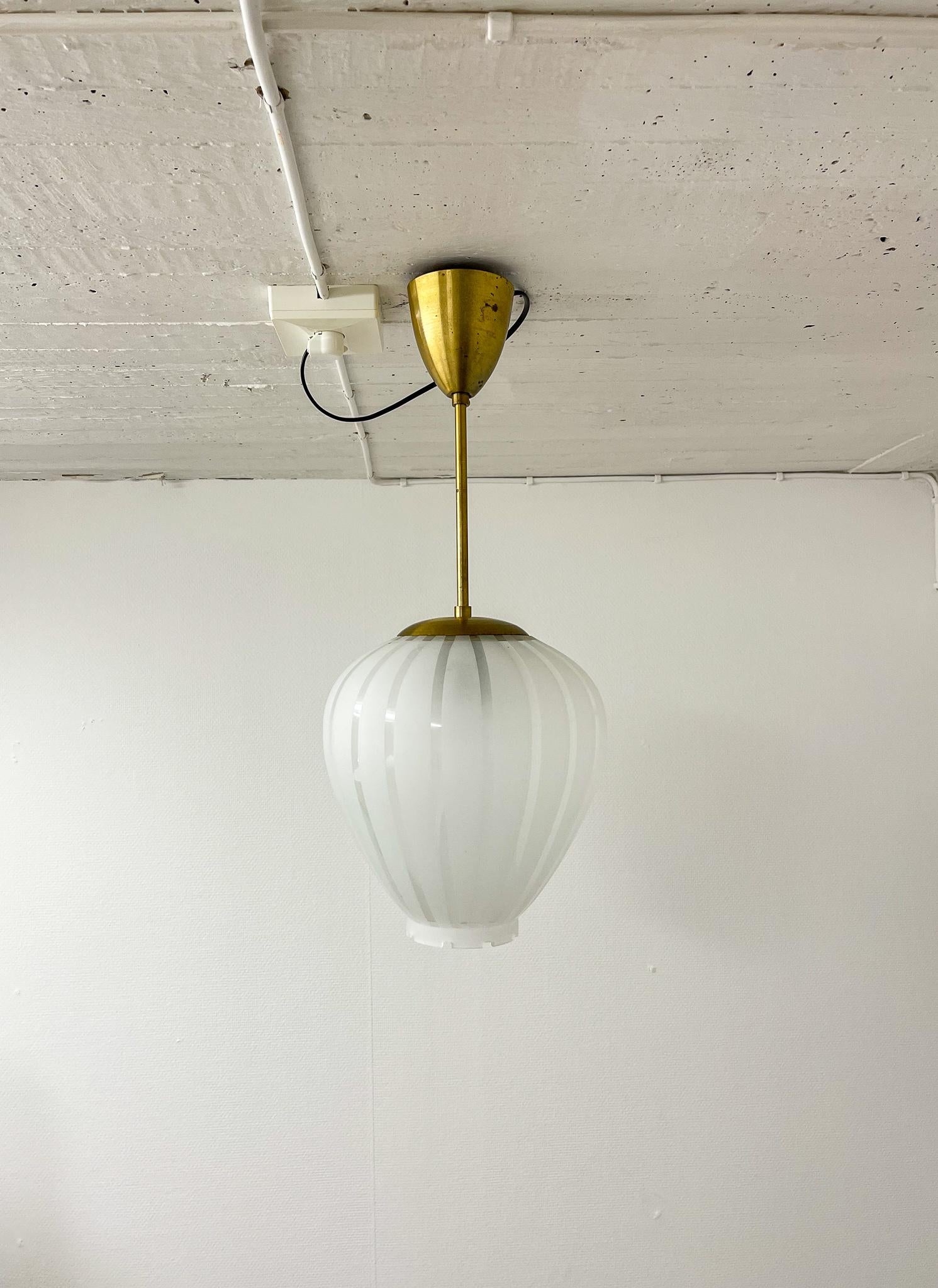 Elegant, middle size rounded pendant in brass and glass produced in Sweden. The frosted glass gives a beautiful and soft light, and the brass parts have a nice natural patina. The bottom of the glass with art deco edges.

Condition: Good original