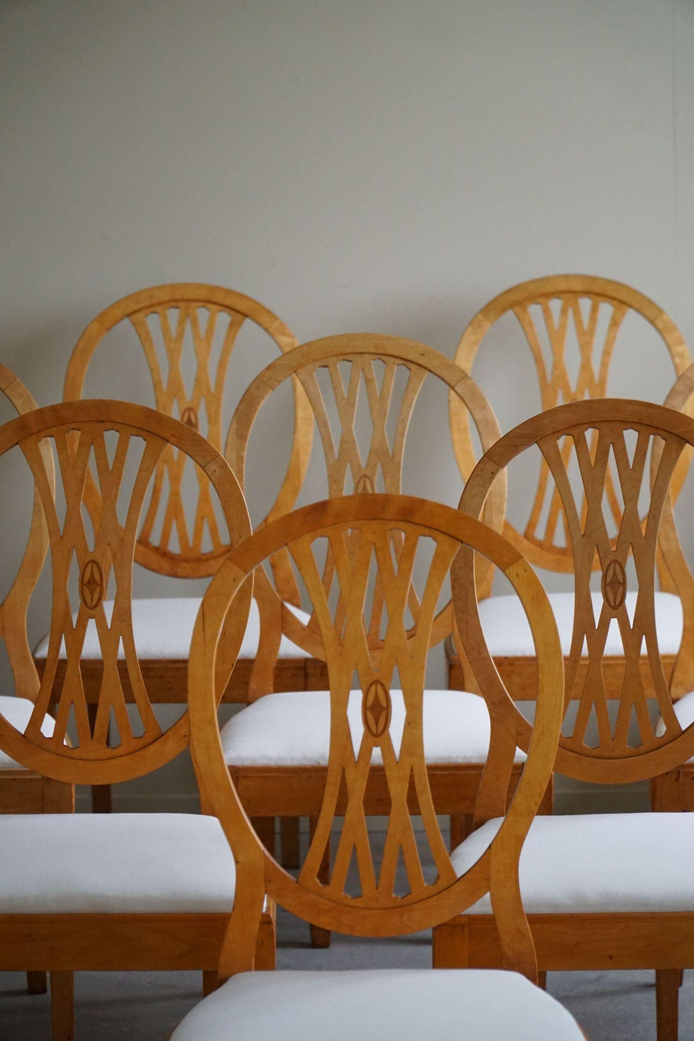 This exquisite set of 10 Art Deco dining chairs exemplifies Gustavian elegance, crafted in the early 20th century by a Swedish carpenter using high-quality birch wood and upholstered linen seats. 
Each chair features a rounded backrest that is both