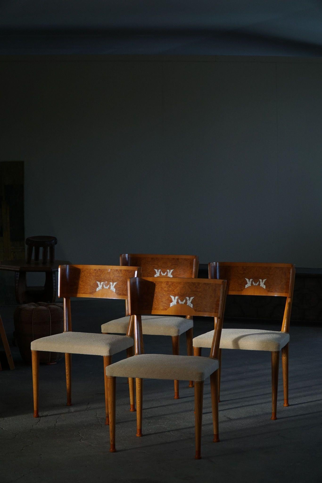 A set of four exquisite dining chairs from the 1930s, crafted in solid elm with elegantly curved backrests adorned in birch root veneer. Each backrest is enhanced with intricate griffin inlays meticulously rendered in bone, a testament to fine