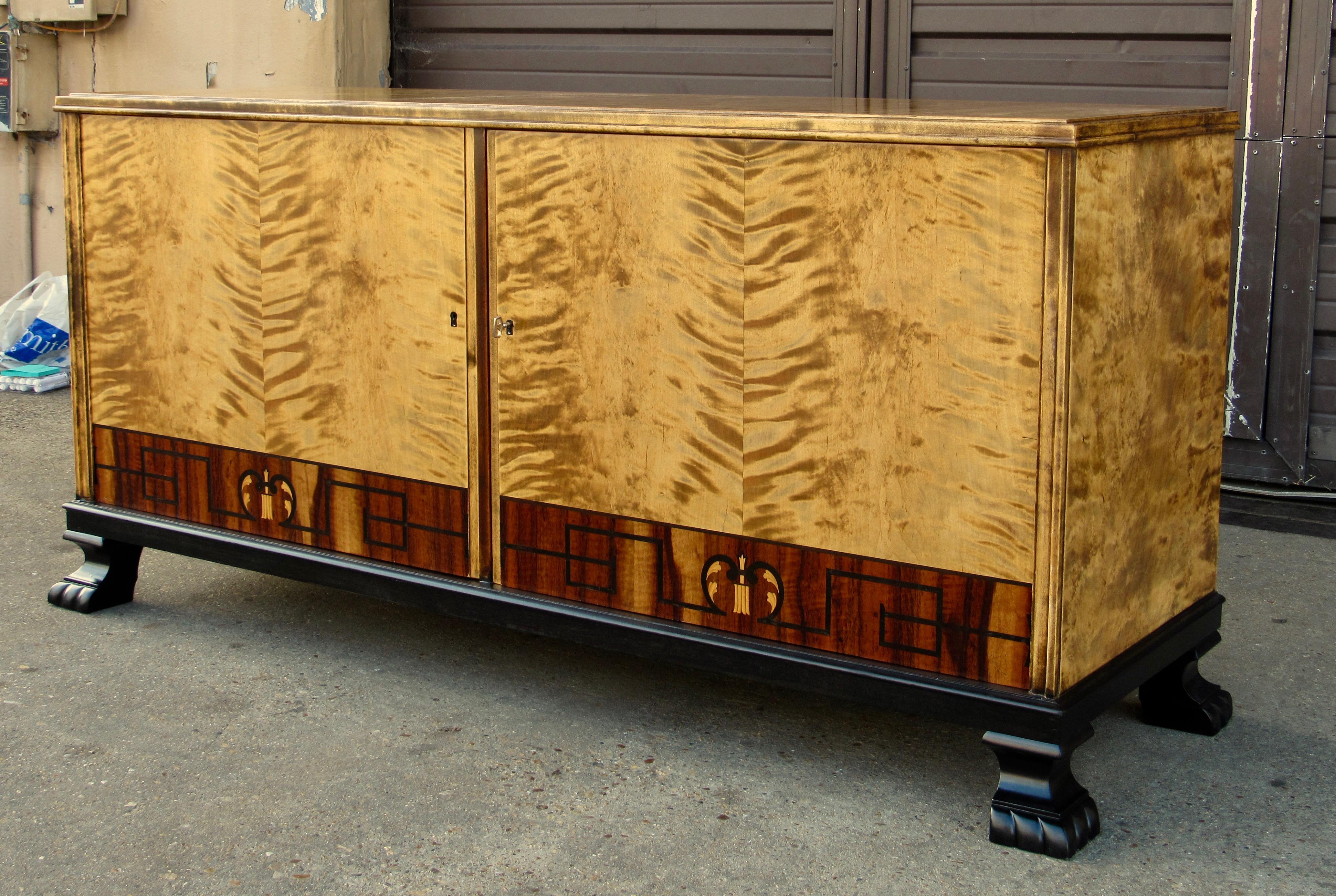 Swedish Art Deco sideboard/cabinet rendered in highly figured, bookmatched golden flame birch. Banded inlay in rosewood and ebony. With ebonized birch wood feet and base. Interior with drawers and removable shelves. This item has just been