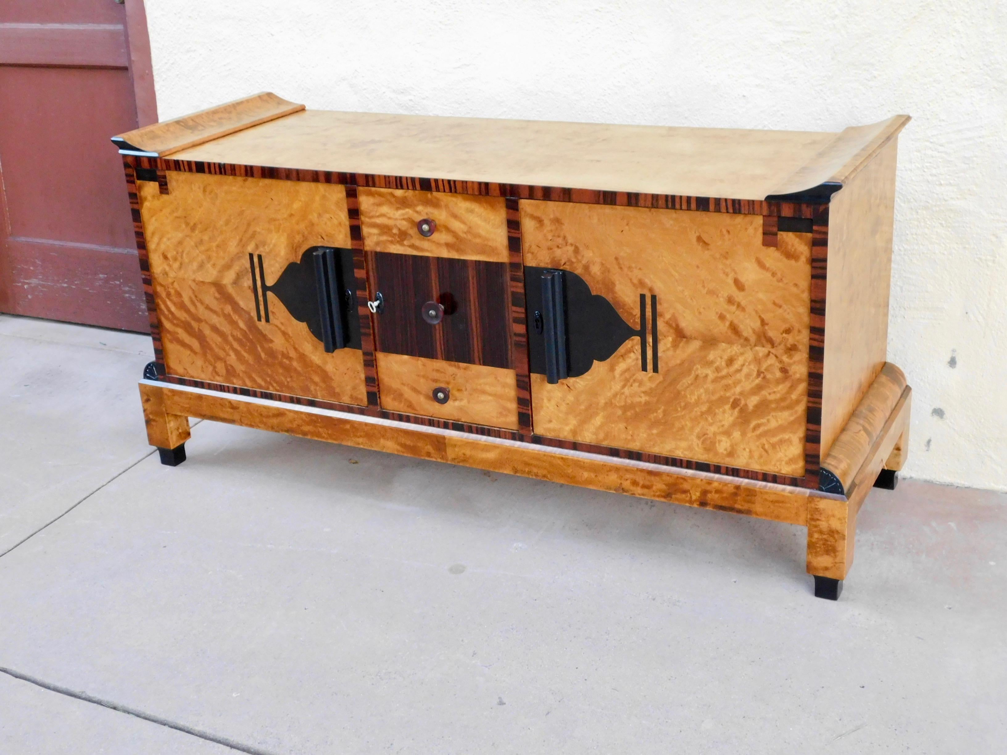 Swedish Art Deco sideboard rendered in highly figured, bookmatched golden flame birch wood. Accented with rosewood and ebony. WIth all original bakelite handles. Interior is composed of drawers and one shelved cabinet, one cabinet without shelf. In