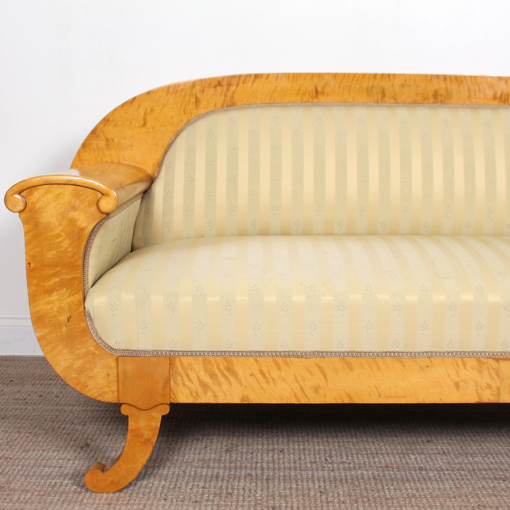 A fine quality satinwood framed Art Deco period sofa.

The burl satinwood marquetry work boasting a magnificent figured grain and vibrant patina.

The arched top and lotus scrolling armrests enclosed an upholstered seat, back and raised on