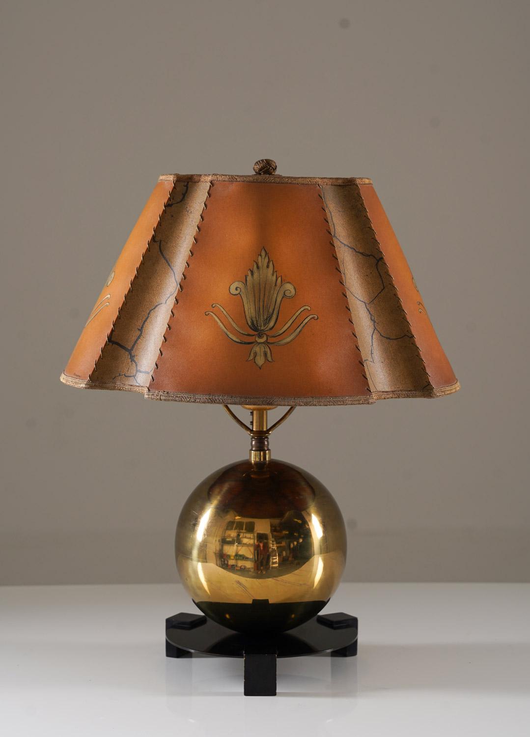 Charming art deco table lamp manufactured by Corona, Sweden, 1930s.
The lamp consists of a large brass sphere with a round black base. The original shade is made of paper with beautiful handpainted ornaments. 

Condition: Very good condition. The