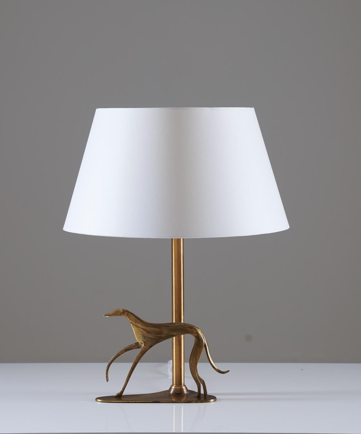 Rare table lamp in brass, most likely manufactured in Sweden circa 1930.
This elegant lamp rests on an organically shaped foot, holding the rod and an ornament in the shape of a dog. The lamp comes with a new high-quality shade in off-white satin