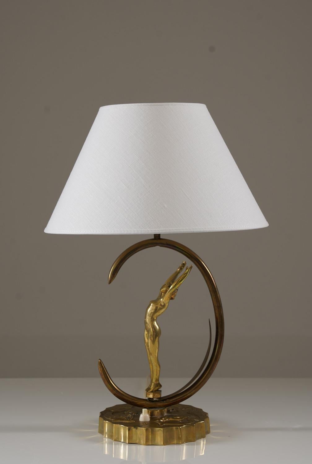 Cette lampe de table suédoise datant d'environ 1940 présente une figure sculpturale en laiton placée dans un cadre en forme de croissant. La base est coulée en laiton avec des bords doucement festonnés et des motifs en relief qui complètent la forme