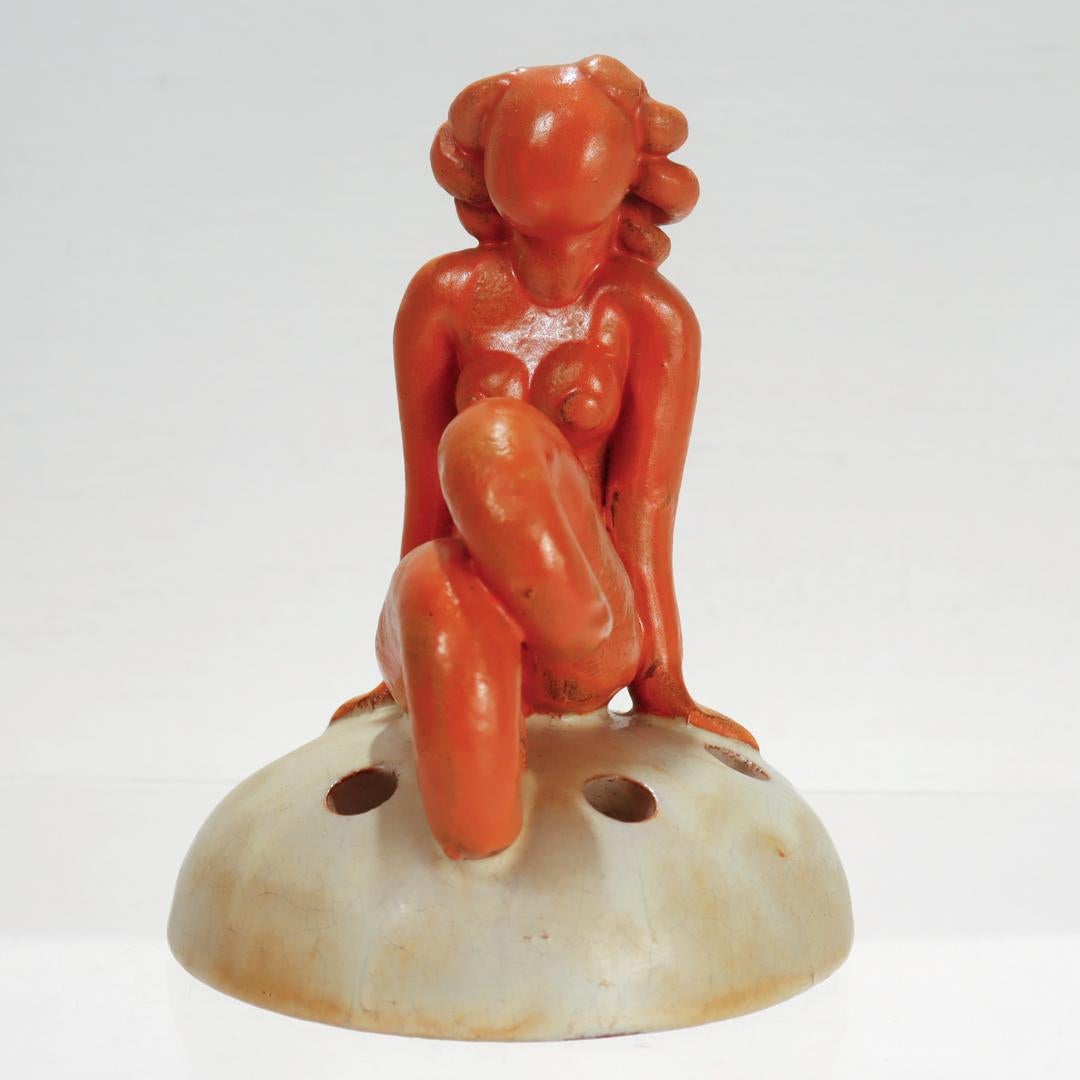 A fine Swedish Art Deco art pottery flower frog.

Designed by Einar Luterkort (1905-1981) for the Upasla Ekeby.

In the form of an orange glazed mermaid figure seated on a vanilla cream colored half sphere flower frog with 6 openings. 

Luterkort is