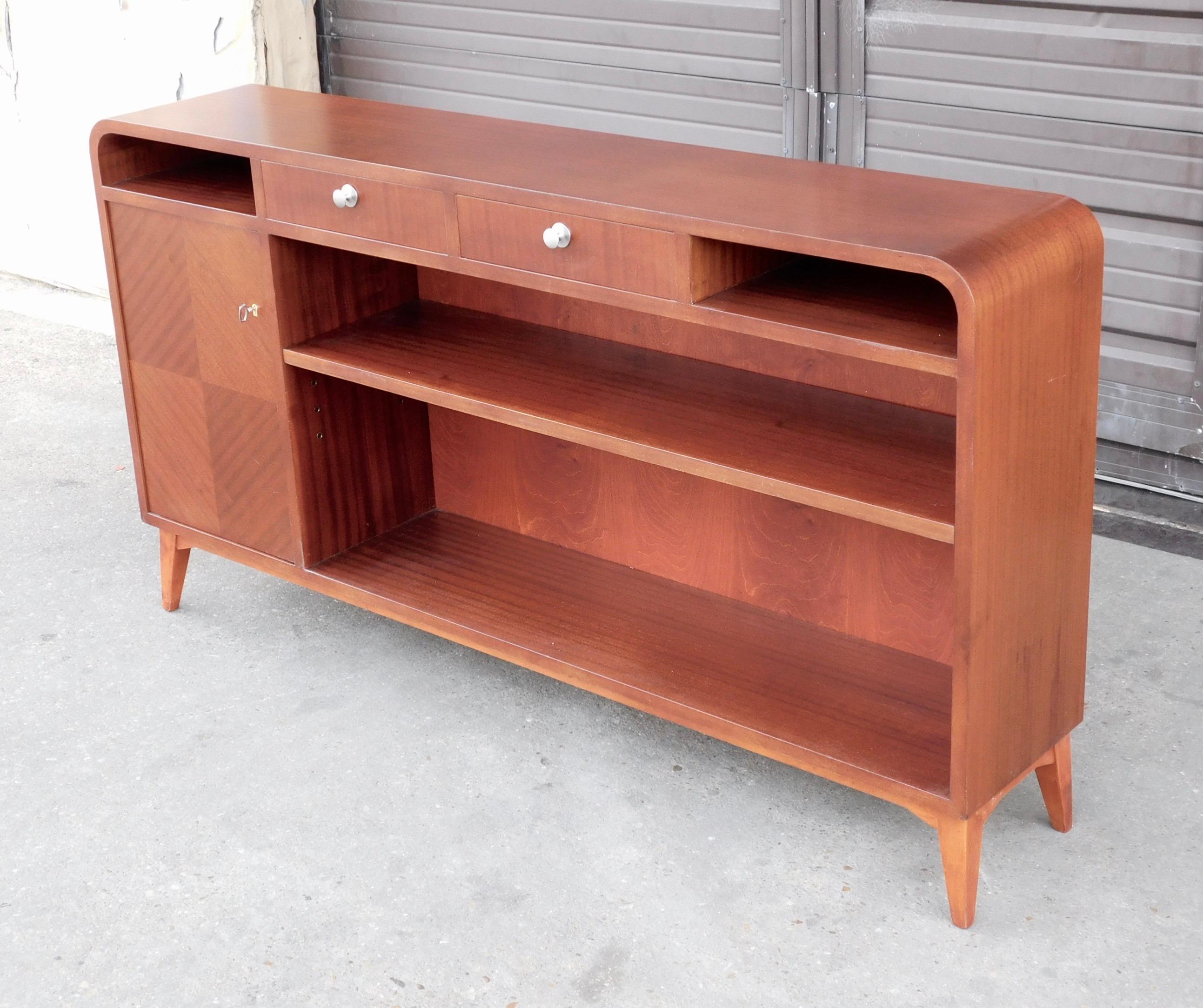 Swedish art moderne bookcase rendered in book matched mahogany.
With one shelf and one interior cabinet.
With original key and original adjustable/removable shelf.
This piece has just had light restoration by our woodworkers and is in great