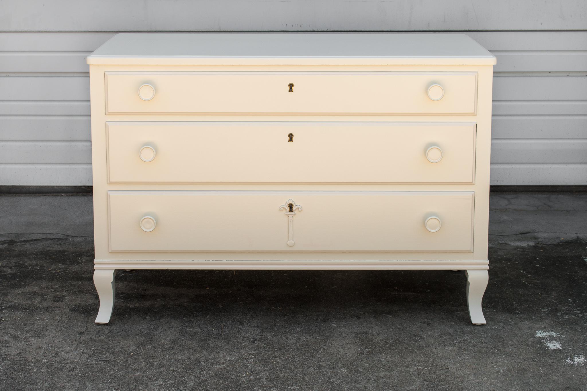 Art Moderne chest of drawers from Sweden, circa 1940. This painted chest of drawers is painted a lovely antique off-white, sits on curved legs and has round drawer pulls and escutcheon ornament on the bottom drawer. All dove-tailed drawers are fully