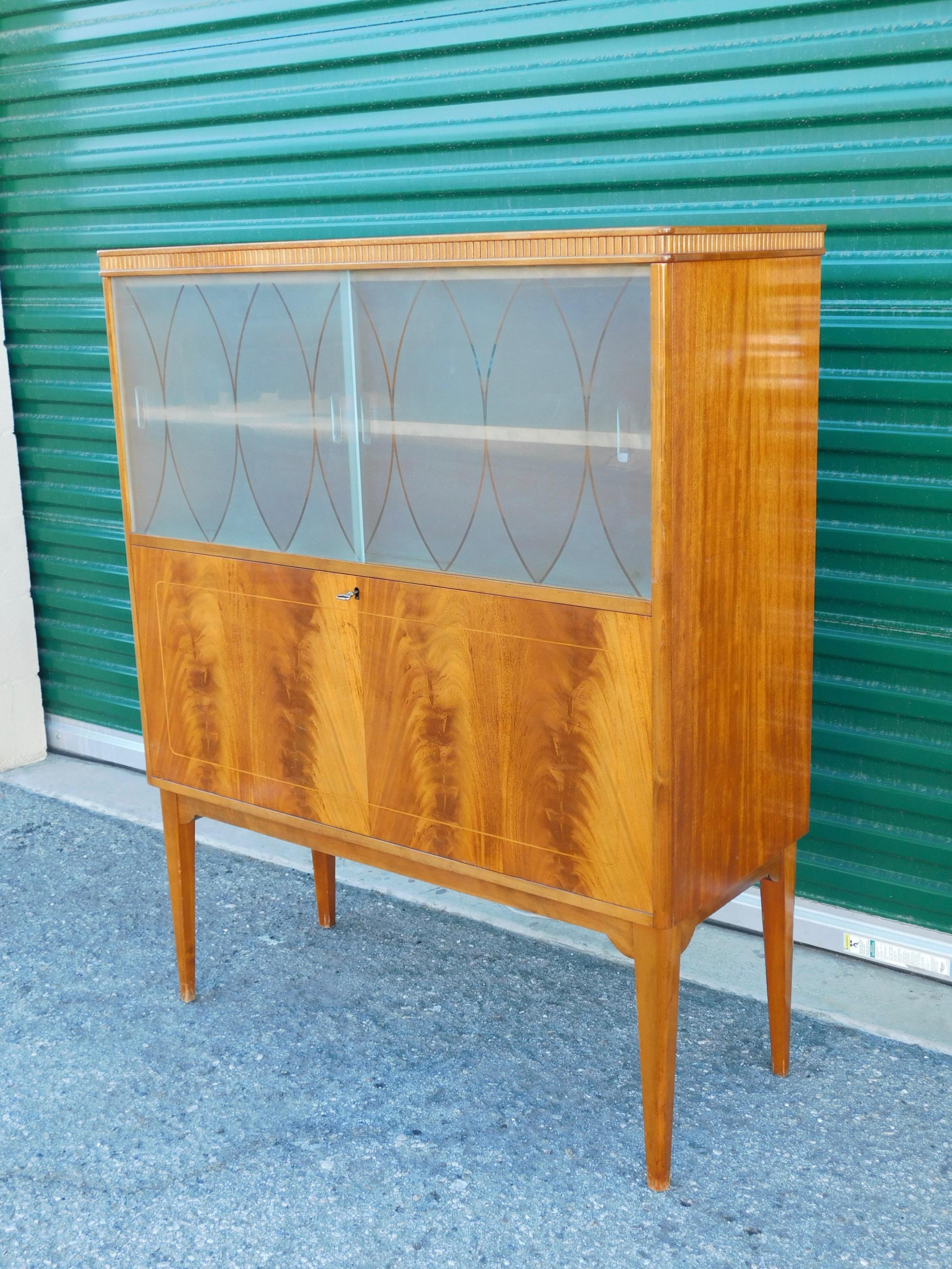 Swedish Art Moderne dry bar in flame mahogany. Rendered in book matched flame mahogany. With original acid etched doors. Interior consists of drawers, and removable/adjustable shelves.
With original key. In original condition. No instability.