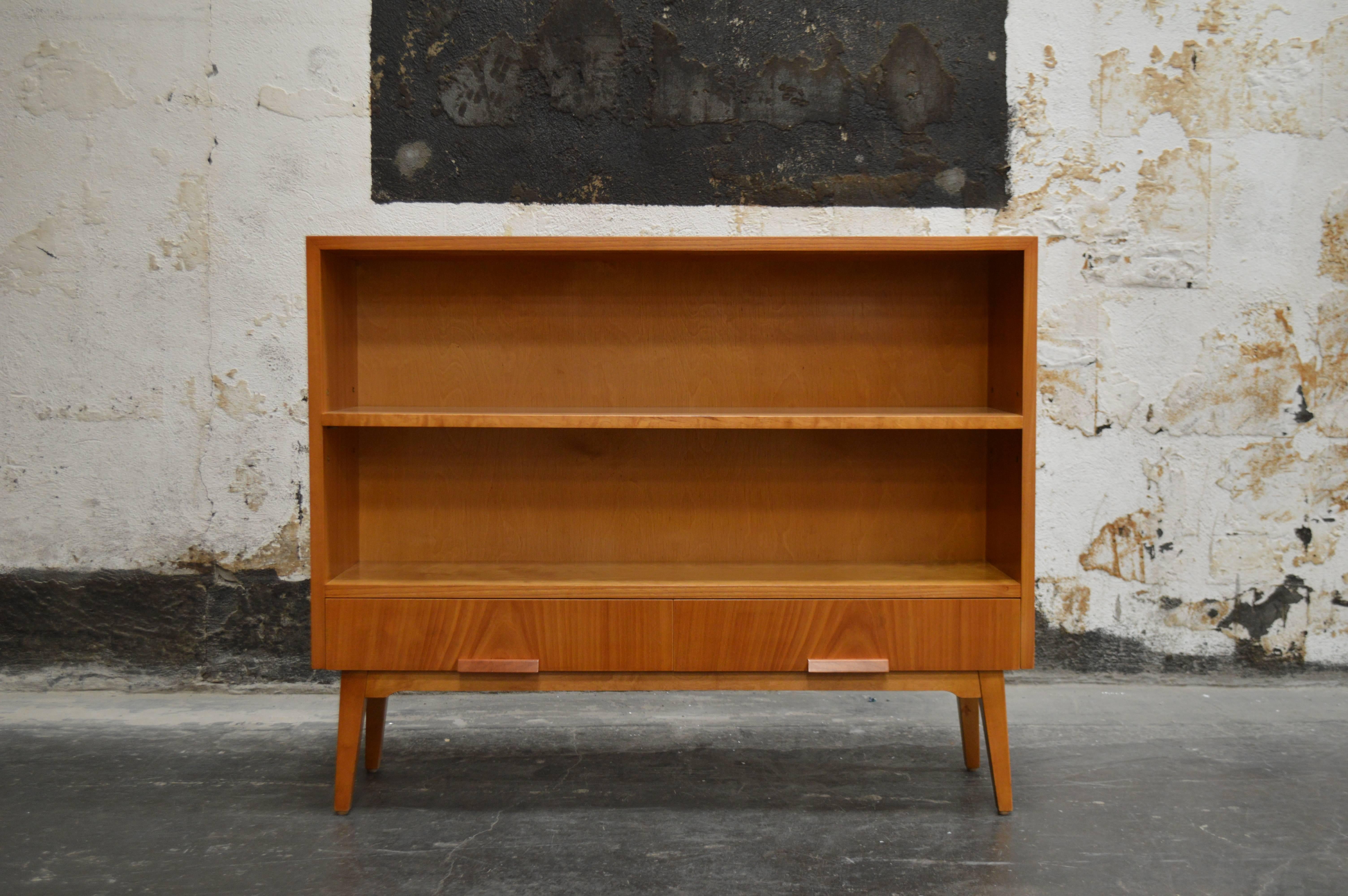 Swedish Art Moderne bookcase in golden elm. Two lower drawers. Modern lines atop handsome tapered legs. 

Approximately ten inches between shelves as shown. Middle shelf is adjustable up or down by up to three inches.