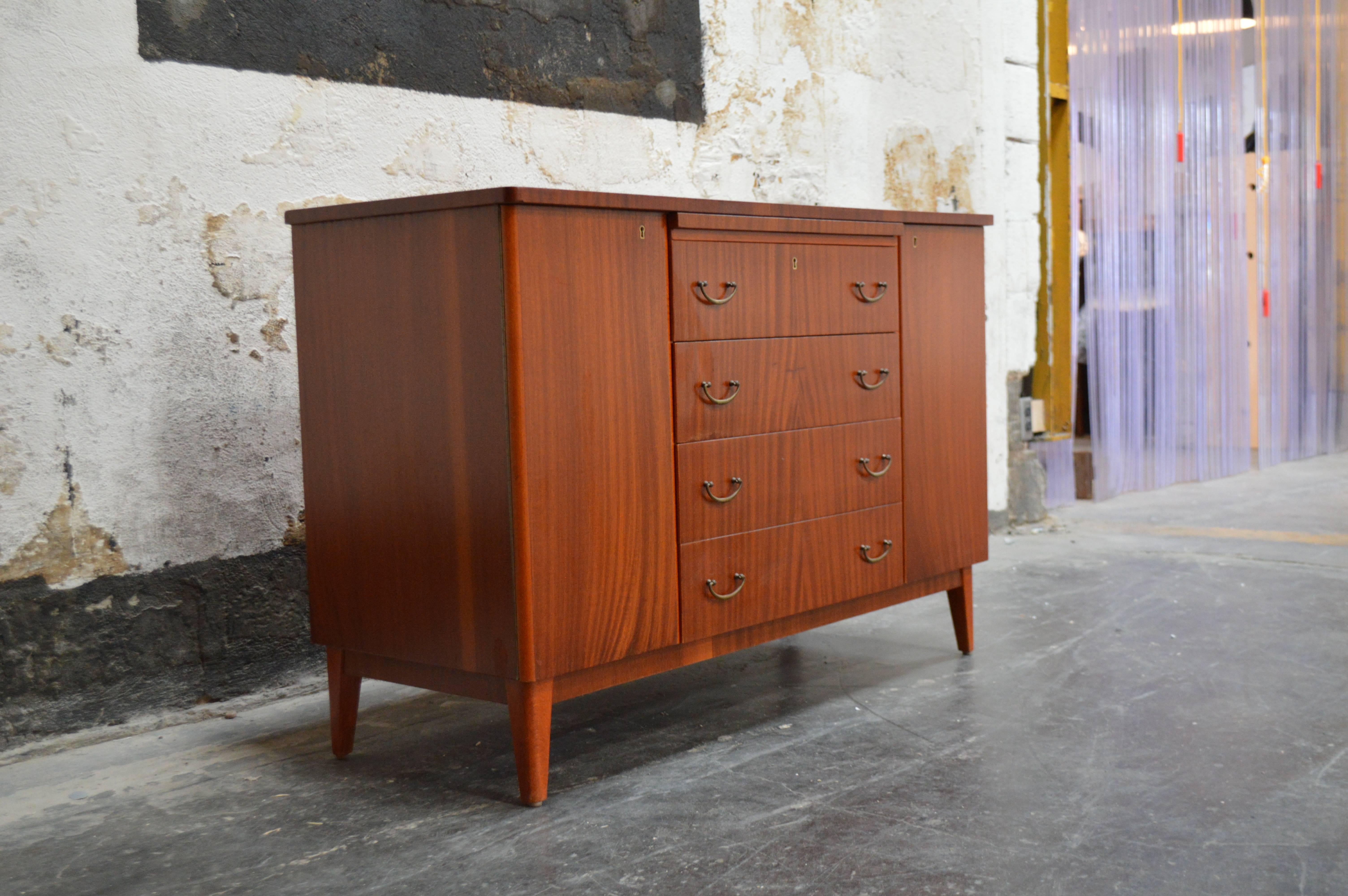 Crafted in ribbon mahogany, this chest/cabinet features a shelf on the left side, five drawers on the right side and four generous drawers down the centre for storage. There is also a pull out shelf on the top for additional serving area. This piece