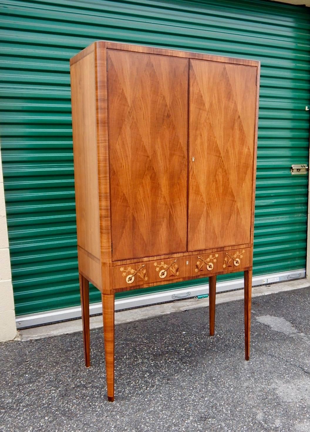 Swedish inlaid storage cabinet, circa 1940. Doors in diamond pattern bookmatched walnut parquetry. Drawer with marquetry in musical instrument theme. There are three original shelves which are removable/adjustable.