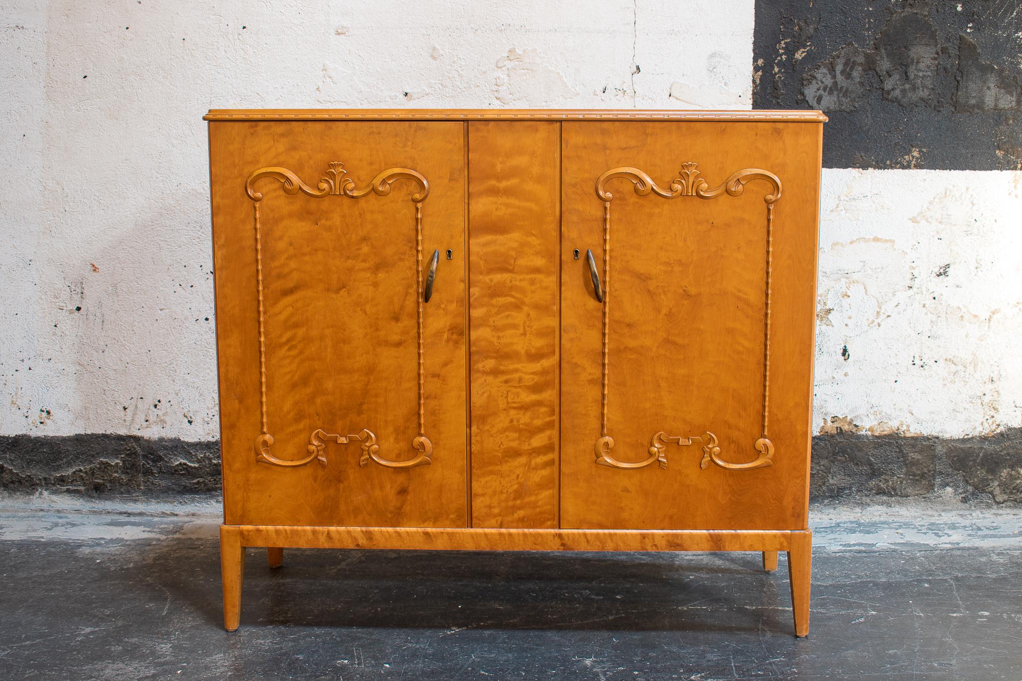Art Moderne buffet cabinet crafted of native golden flame birch with carved details. This gorgeous wood has mellowed to a rich amber color. This storage piece opens to reveal a golden elm interior with four shelves and two drawers. Key included.