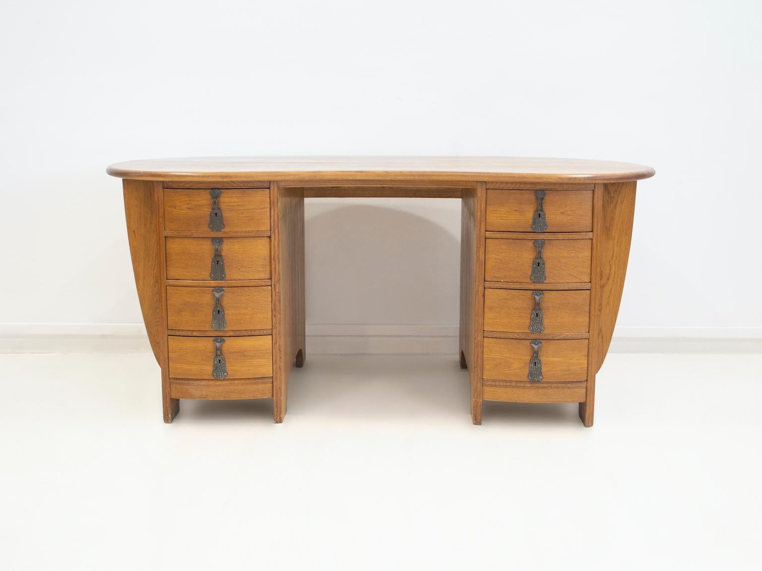 Kidney-shaped oak writing desk with double chest of drawers with 8 drawers on each side. Wrought iron handles. Sides with magazine racks.