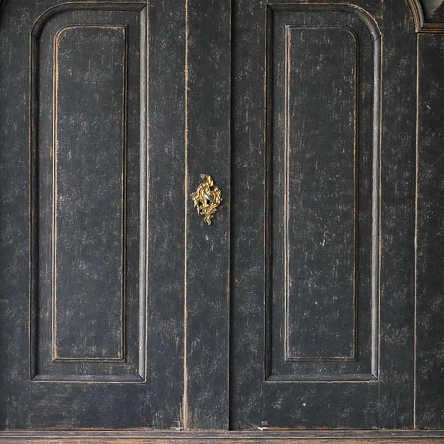 Une armoire d'époque rococo avec fronton sculpté décoratif. Deux portes avec des détails décoratifs sculptés s'ouvrent sur des étagères de rangement, et en dessous, deux tiroirs courts et deux longs. Cette pièce est d'époque mais sans la