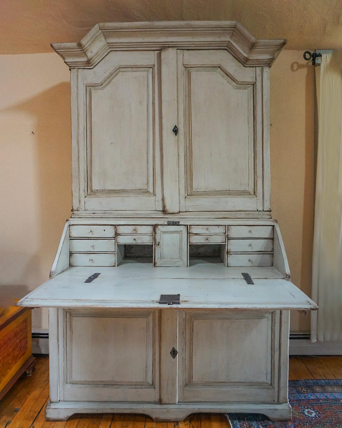 Early Swedish secretary, circa 1800, in two parts. The upper section has a bold cornice with beautiful form over a pair of raised panel doors. Inside are three fixed shelves, the top one having a curved shape with notches for spoons. The lower