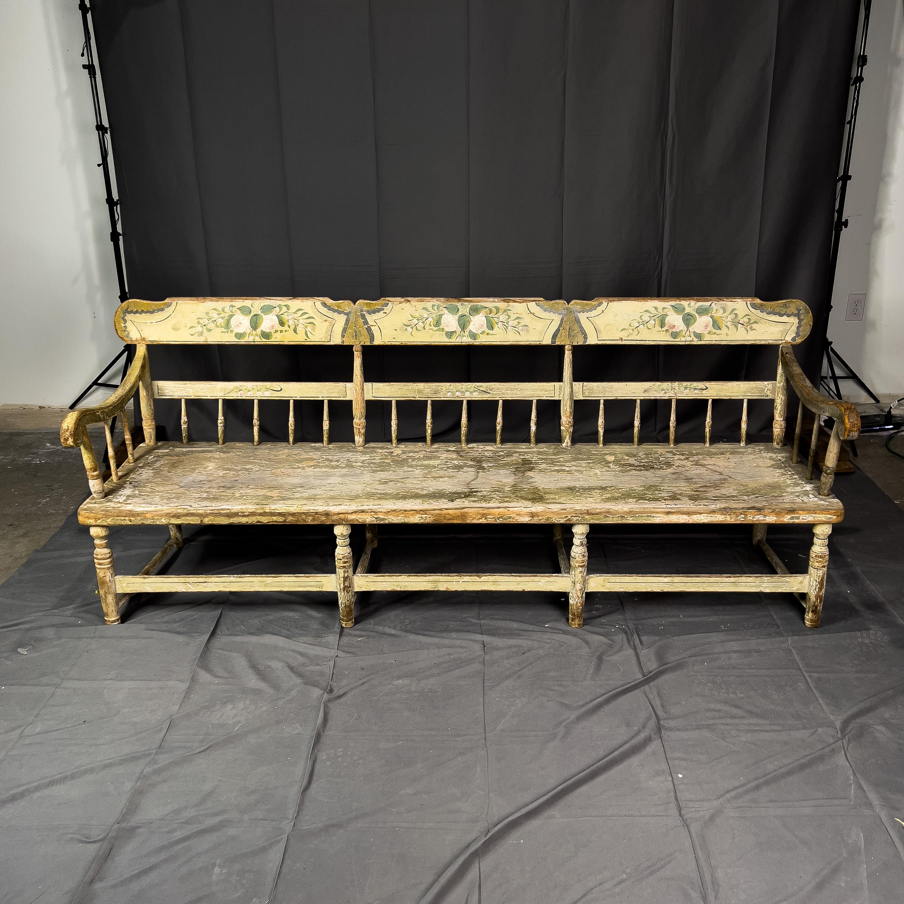 Swedish bench half-spindled and hand-painted. The bench has a half row of spindles on three sides above a long plank seat and is raised on eight tapering legs joined by spindled stretchers. This piece makes a very charming and decorative statement.