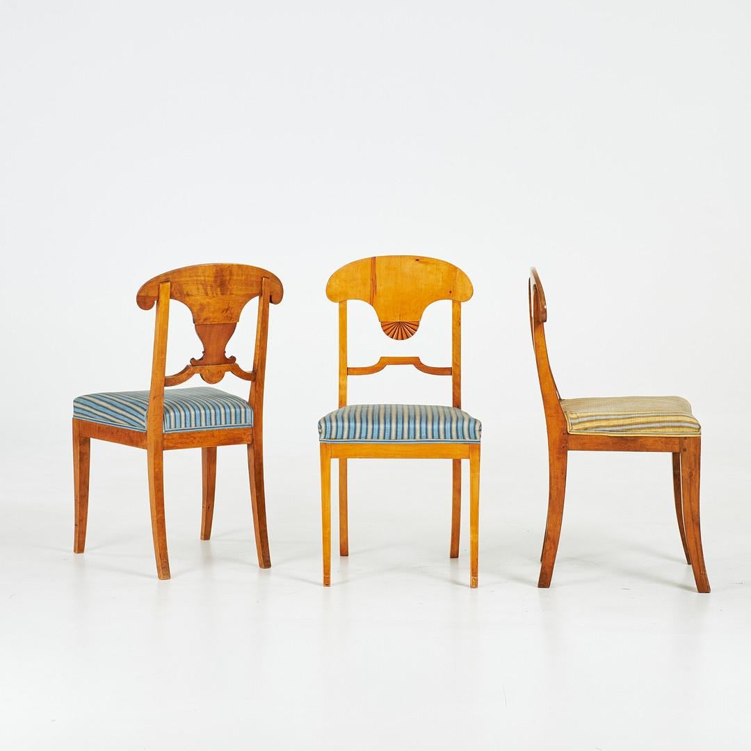 Sillas de comedor Biedermeier en raro conjunto mixto de 8 suecas antiguas con chapas de abedul dorado flameado con el característico respaldo curvado, diferente motivo central tallado y patas delanteras graciosamente curvadas. Magnífico nivel de