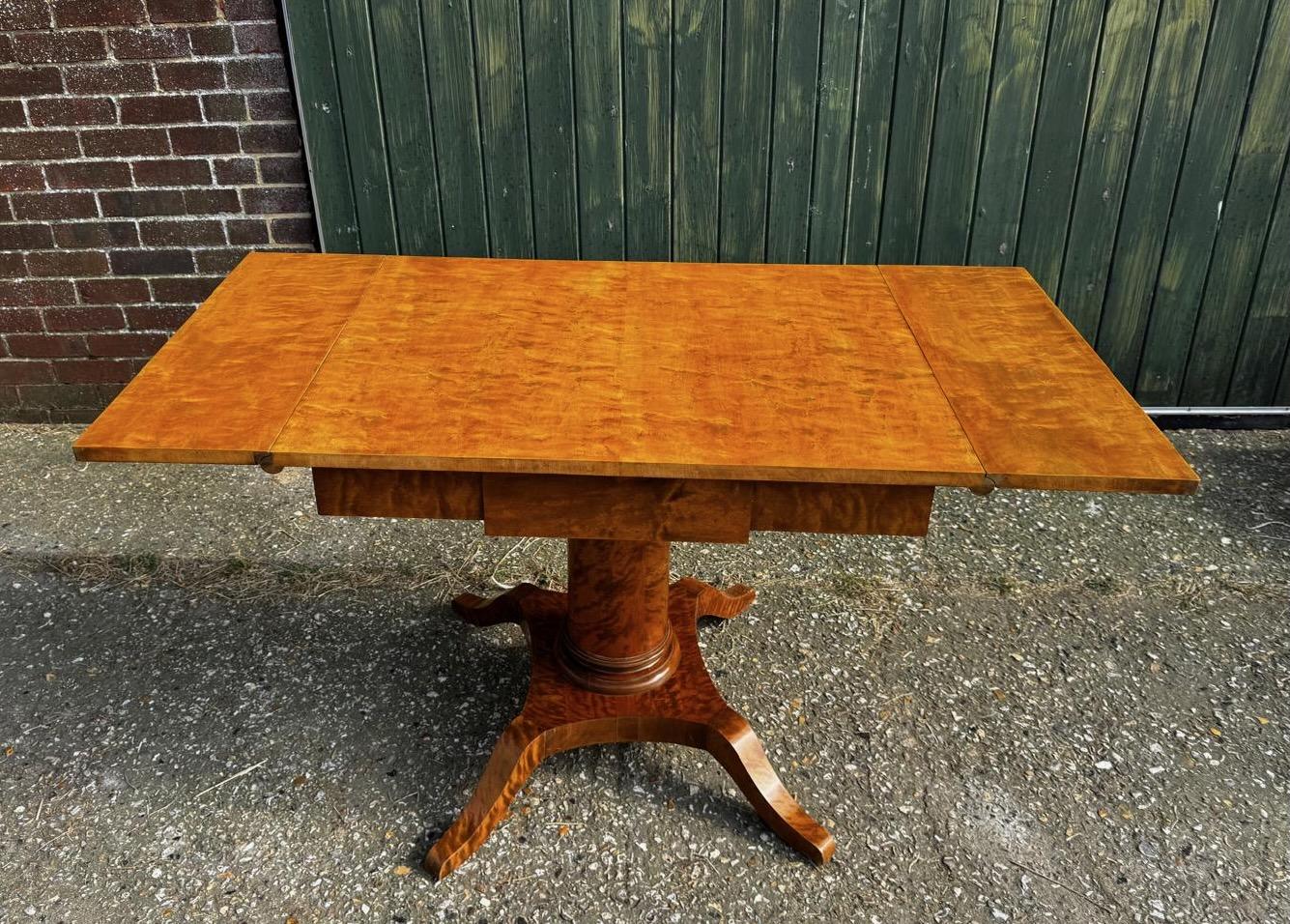 Antique Swedish Biedermeier drop-leaf table in stunning tiger stripe and quilted golden birch veneers and four elegant curved feet.

The pedestal column in particular features beautiful swirls in the wood and also on the feet.

Table wings are