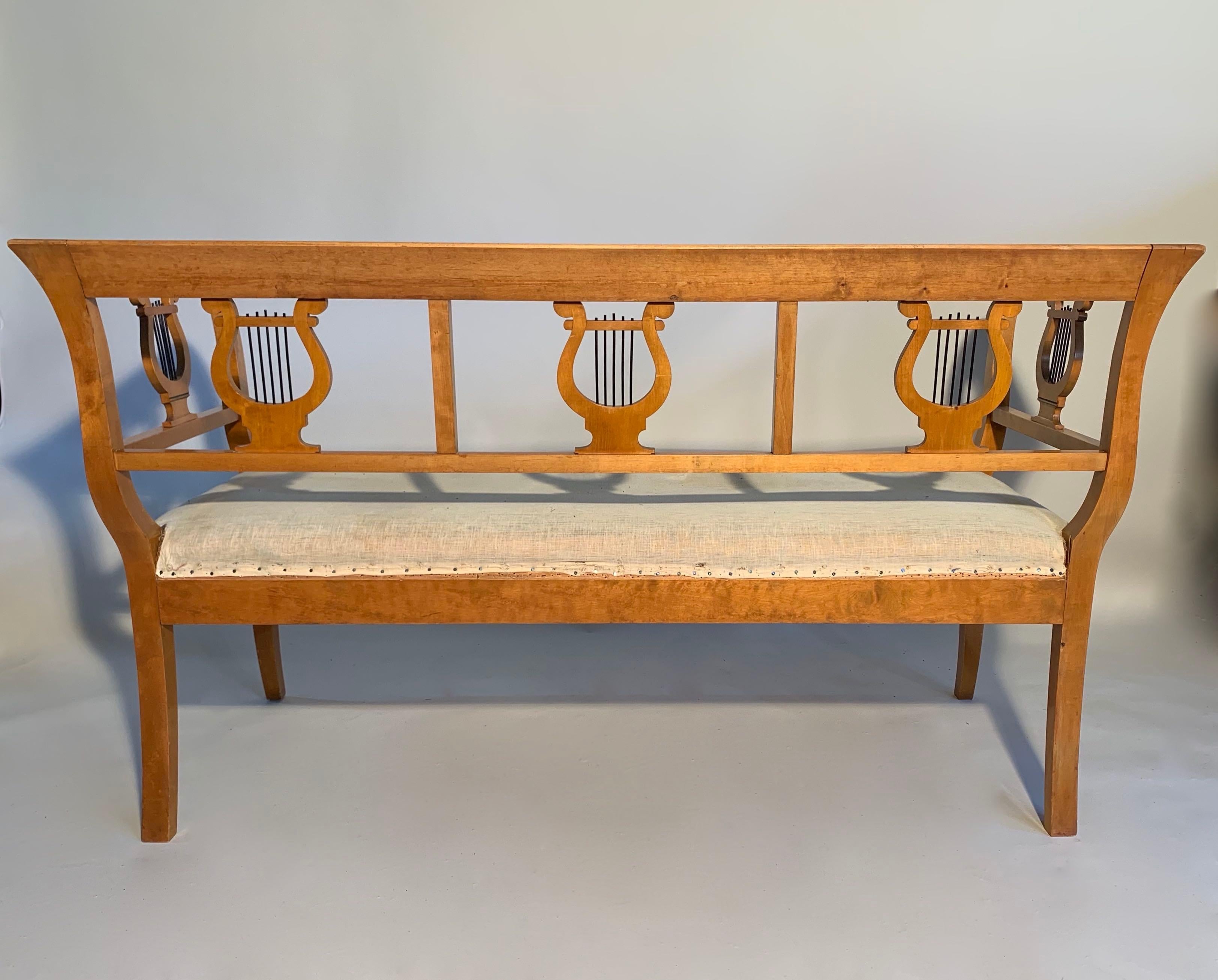 Swedish birch Biedermeier sofa with lovely small proportions. Decorated with classical hand carved Lyres to the back and sides. The seat has the original calico. New upholstery is included in the price. This is a very nice example of these hard to
