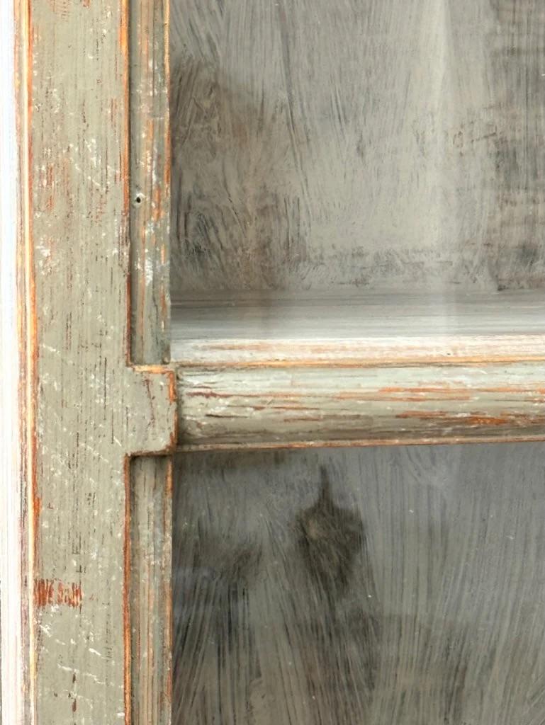Vitrina de porcelana pintada de azul sueco, hacia 1800, en dos piezas, de forma ligeramente redondeada, la parte superior en forma de bonete con frontón de arco roto moldeado sobre puertas acristaladas que se abren para revelar estantes, la parte