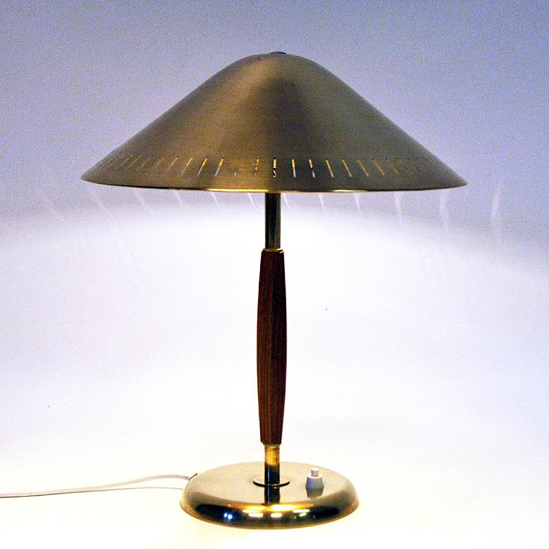 Lovely tablelamp with a round brass shade on a elm pole model 15296 made by Harald Notini, Böhlmarks Lampfabrik, Sweden, 1940s. The brass footbase has a light switch and a finely sculpted wood handle on a brass rod. The brass shade is perforated in