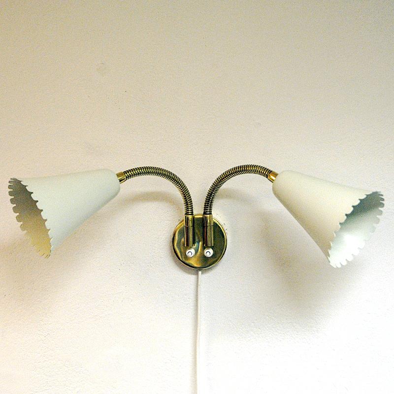 Brass and metal adjustable wall lamp with two lights of model 8661 for Böhlmarks Lampfabrik - Sweden 1940s. Coneshaped  creamcolored-lacquered metal lampshades with rifled edges. Goseneck function with adjustable metal arms to place the light shades