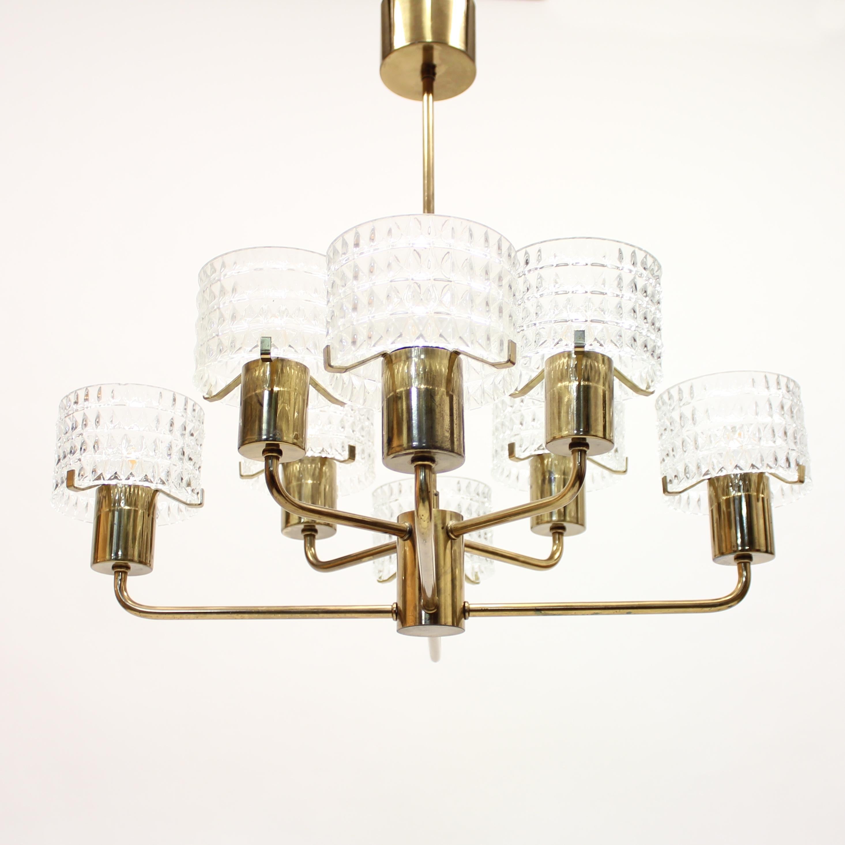 8-light brass chandelier with glass shades made in Sweden in the 1960s. The shades rests on three brass holders that sits on top of every lamp holder. An extra glass shade is included and is a good thing if one of the shades should break. It also