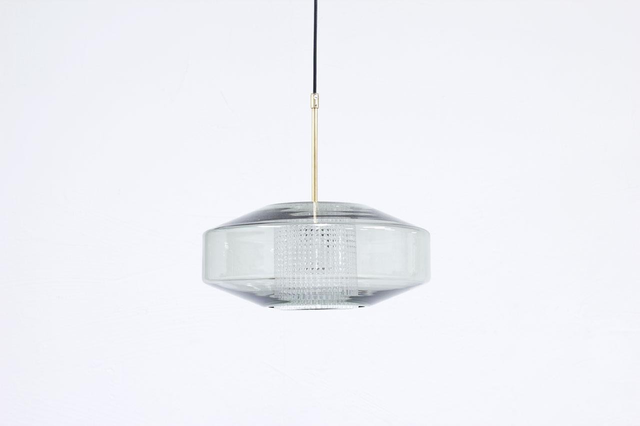 Pendant lamp designed by Carl Fagerlund
for Orrefors. Produced in Sweden during
the 1960s. Flattened sphere shape in light
grey tinted glass with a cylinder internal
diffuser in clear pressed glass. Fittings
made from polished brass. New