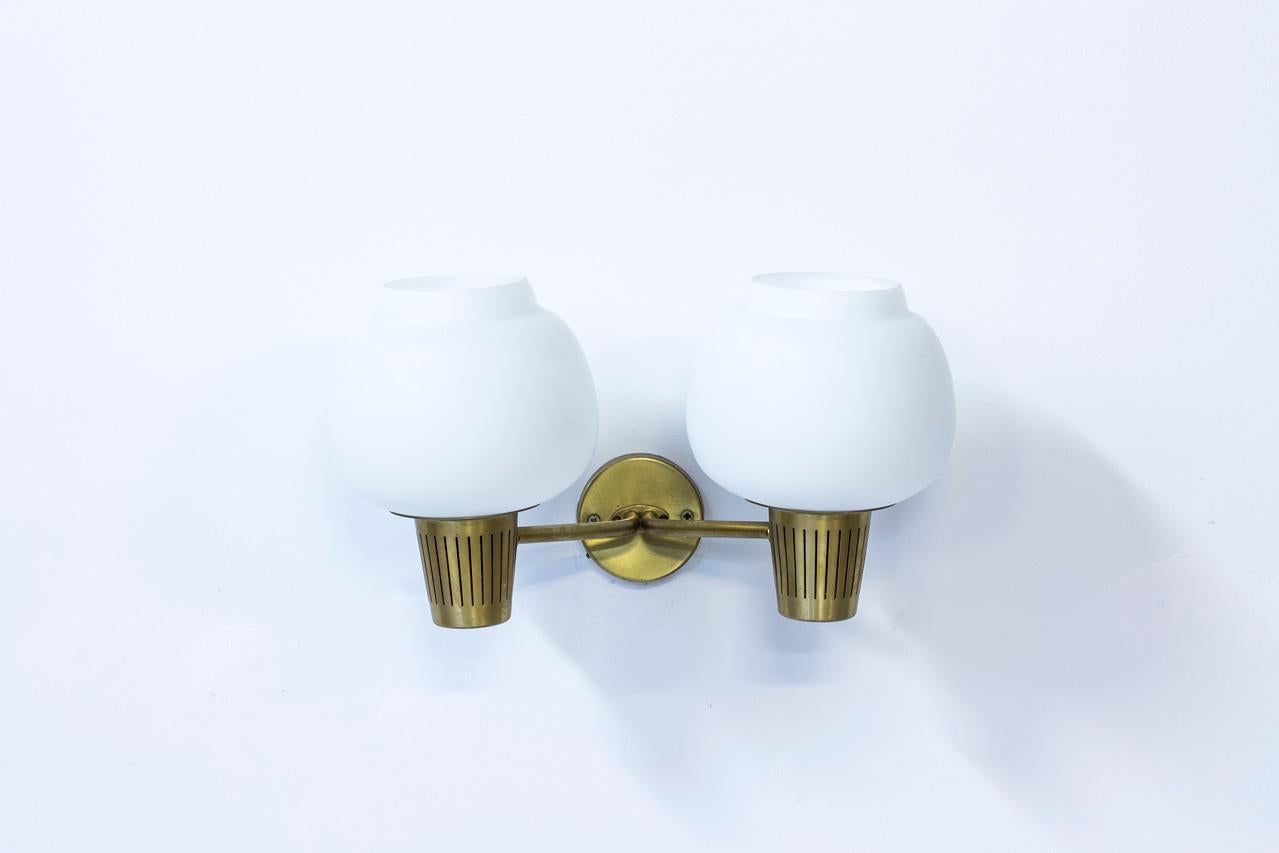 Large two headed wall lamp designed by Hans Bergström for Ateljé Lyktan during the 1950s. Polished brass wall mount with two opaline glass diffusers.