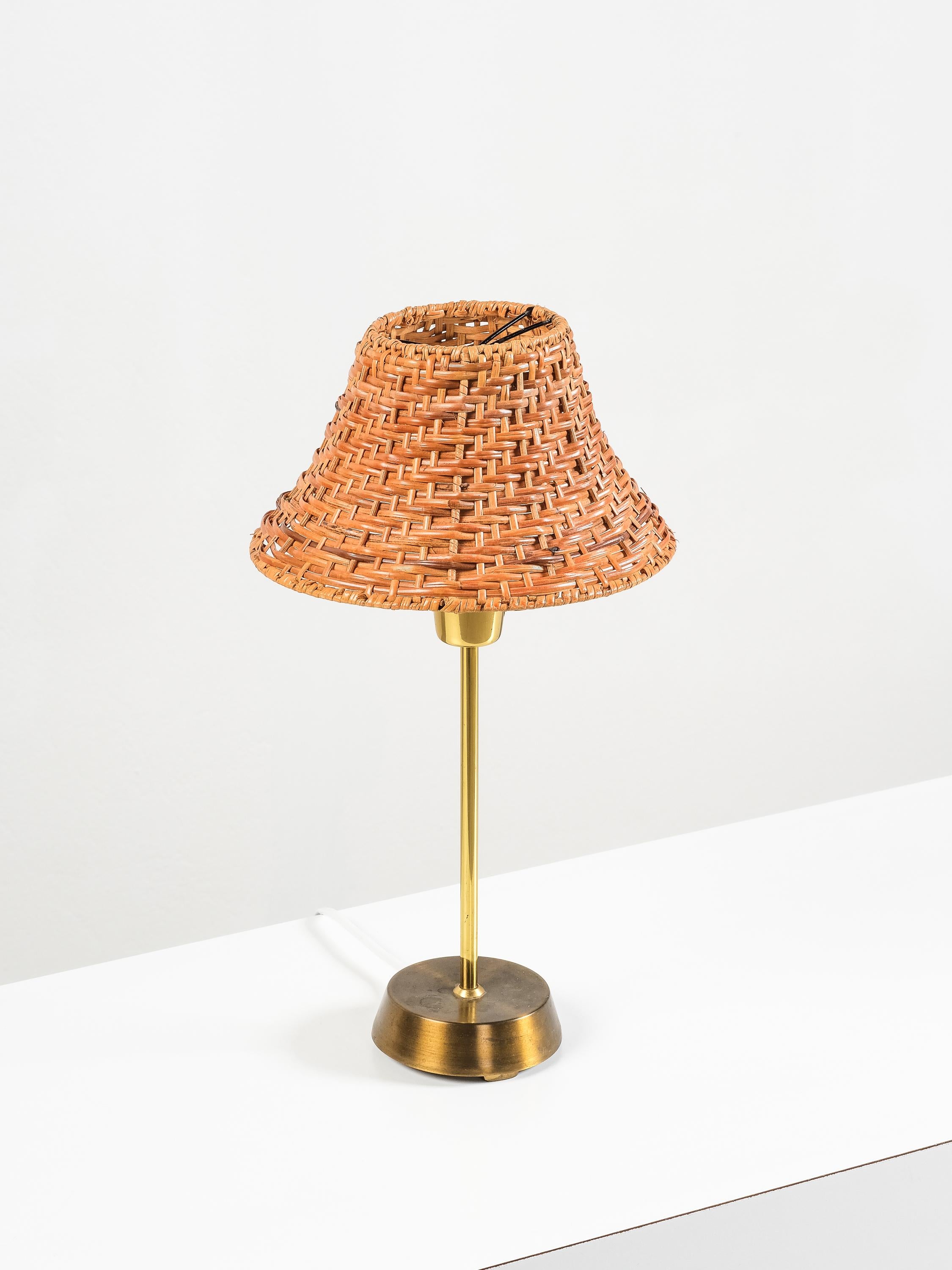 This charming Swedish brass table lamp was produced by EWÅ Värnamo in the 1960s and exemplifies the era’s warm, natural material palette and Scandinavian modernist sensibility. The sleek brass stem and weighty base are paired with a handwoven rattan